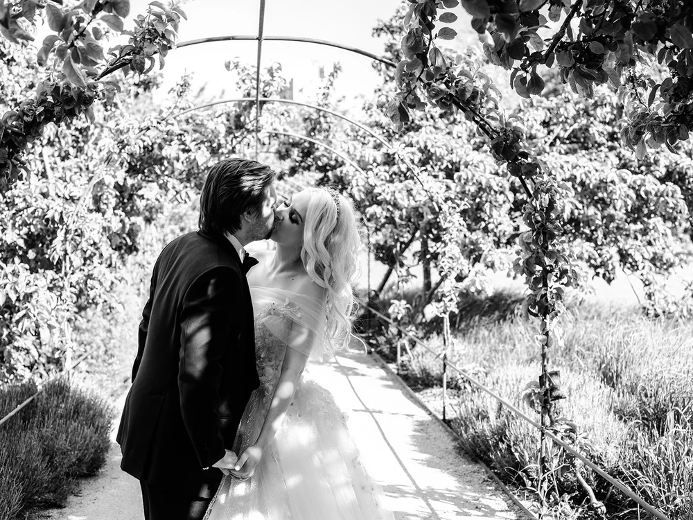Bride and groom kissing under a garden arch