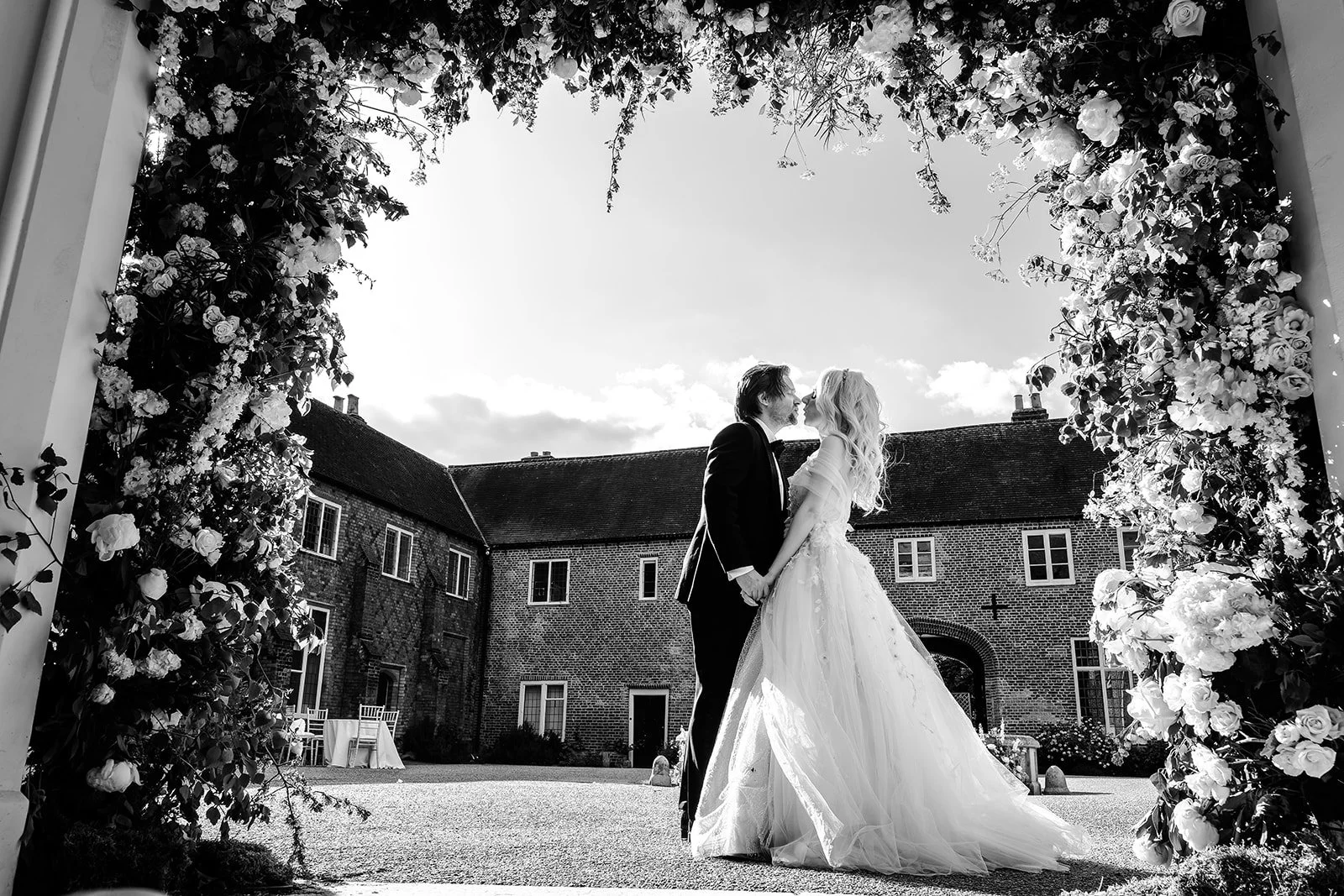 Caroline and Alex kissing beneath a flower arch at Fulham Palace