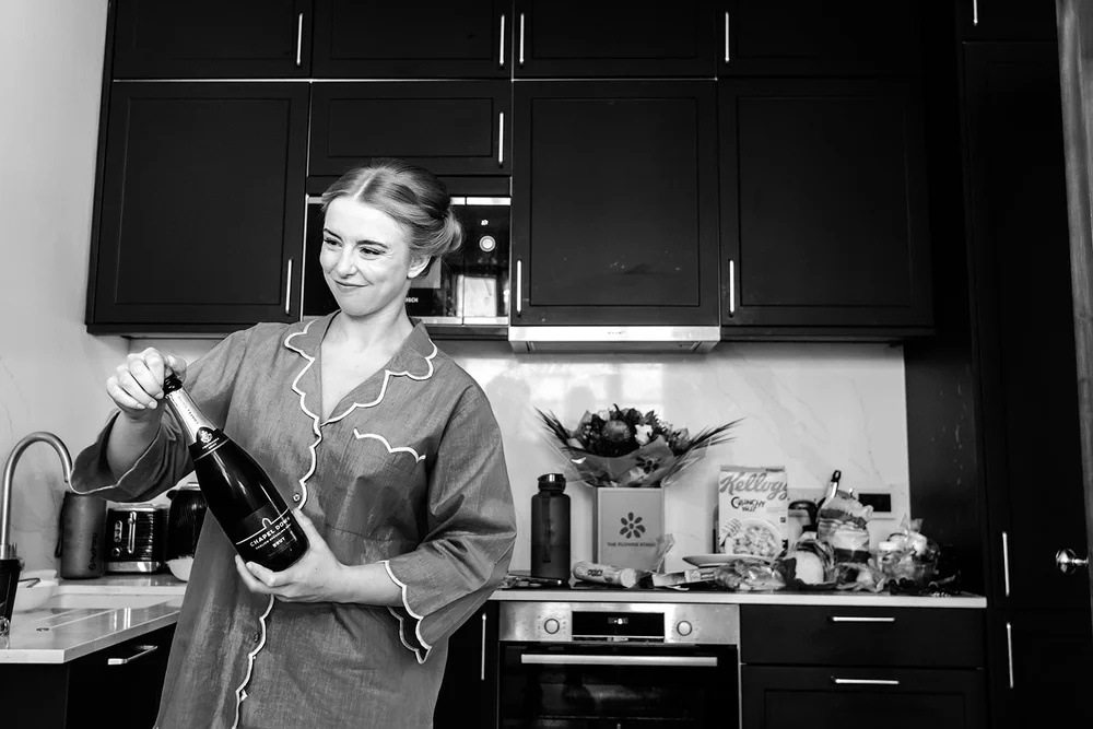 Grace opening a bottle of champagne in her pyjamas on her wedding morning