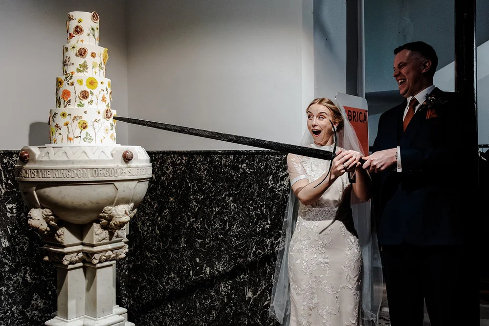 Grace and Jordan cutting their flower covered wedding cake with a sword at Fabrica Brighton