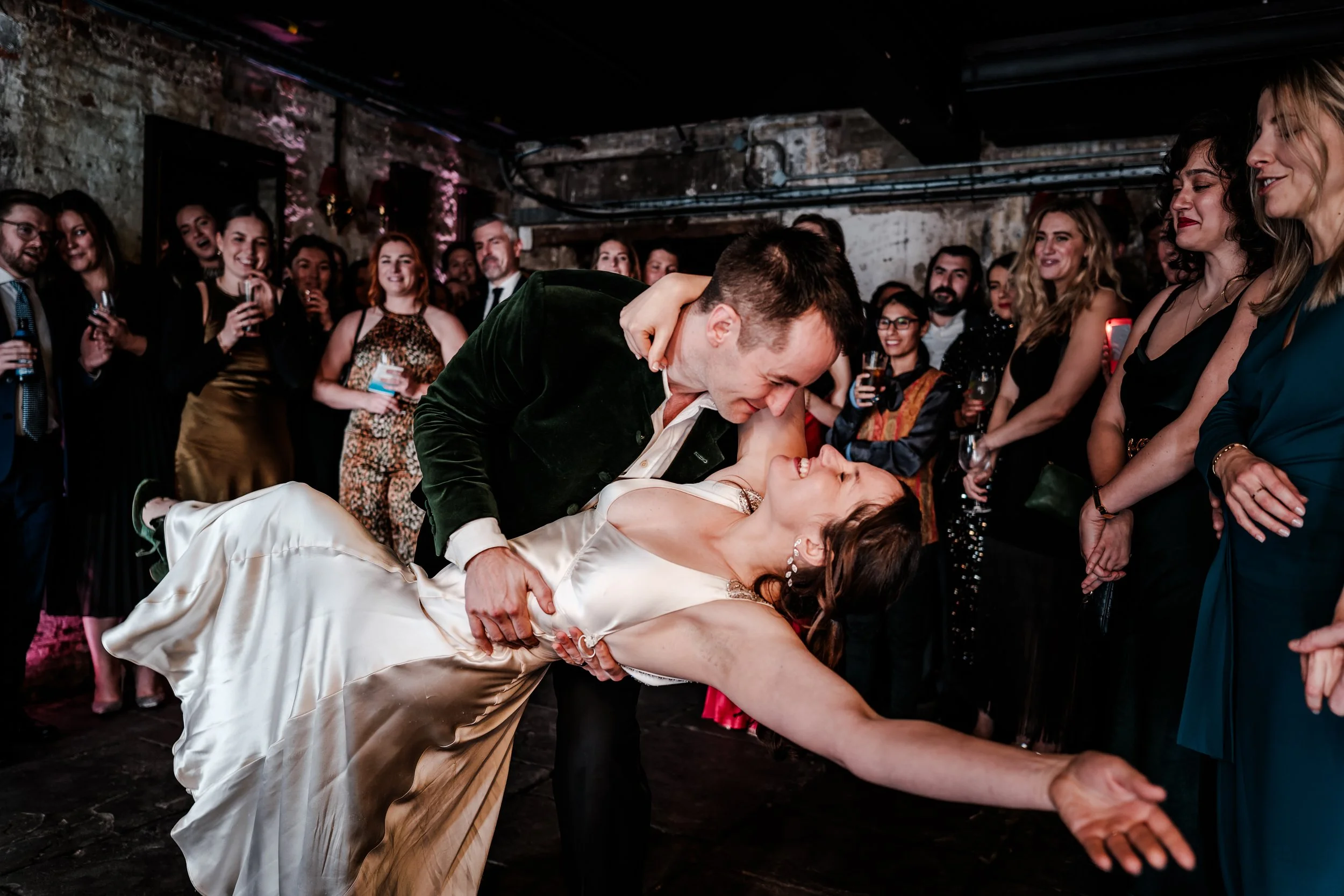 A couple dancing at a wedding reception surrounded by friends and family.