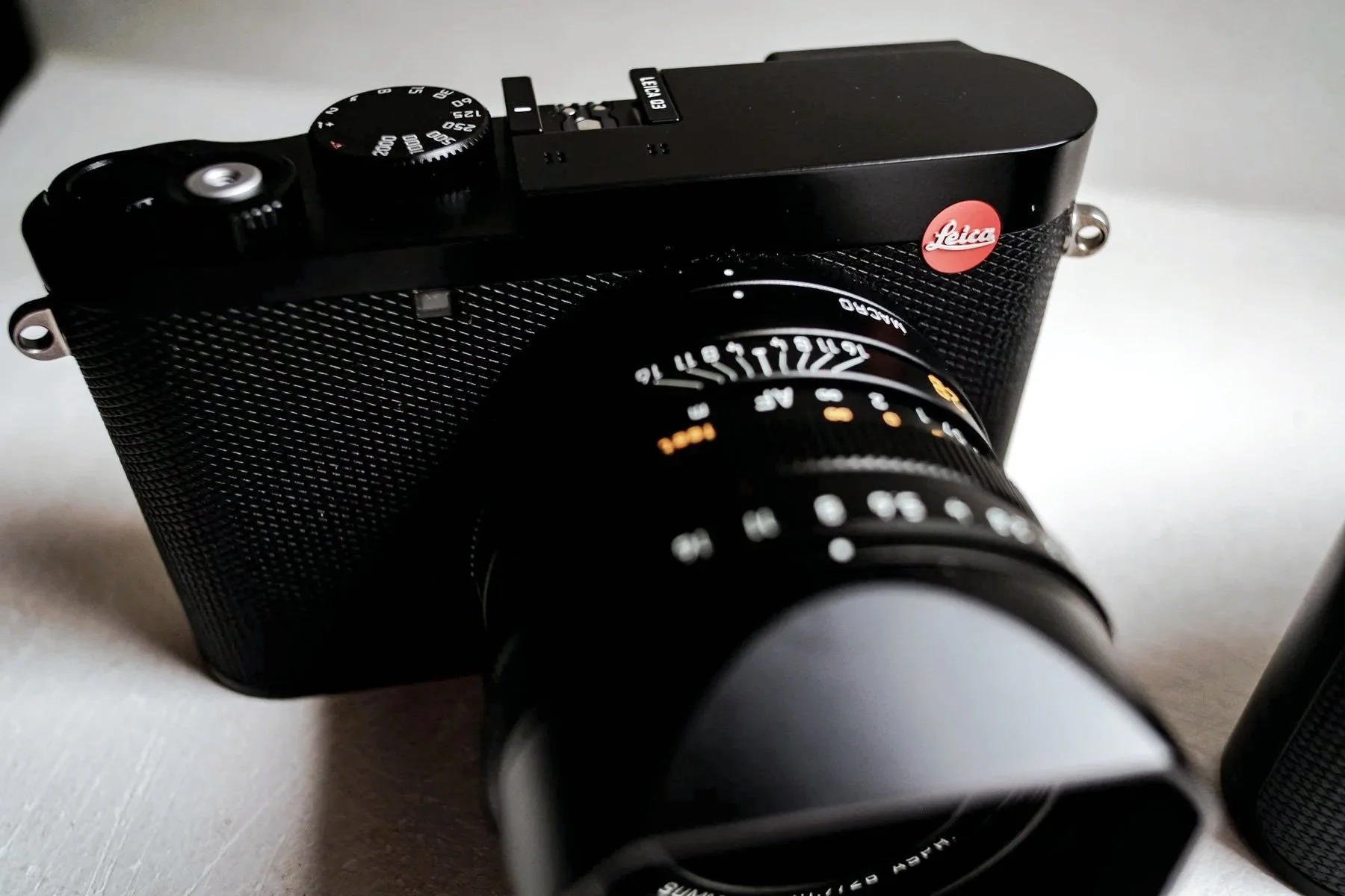 Close-up of a Leica camera with a zoom lens attached, placed on a surface.