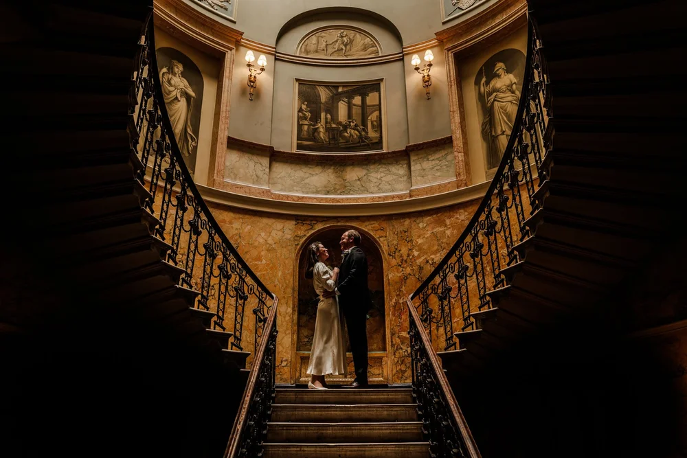 Bride and groom descending the grand staircase at Home House Marylebone London &mdash; elegant wedding photography by Oliver Holder