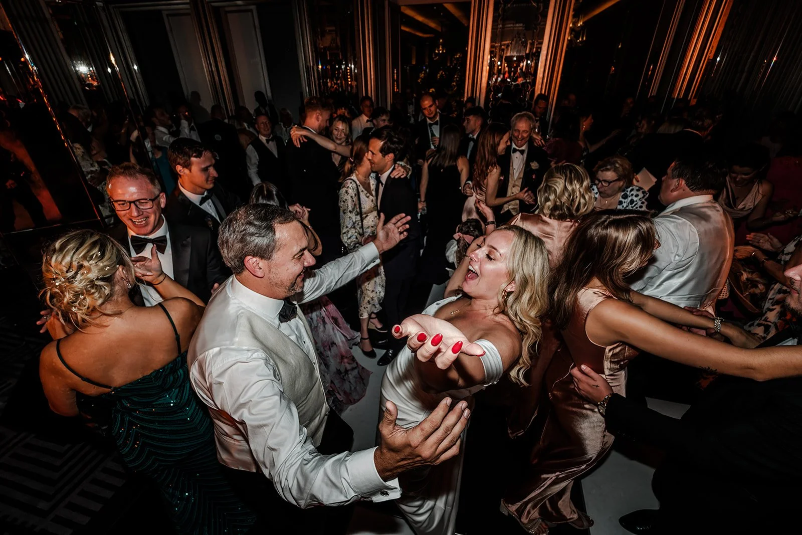 People dancing and socializing at a formal party or event in a dimly lit venue with mirrors on the walls.
