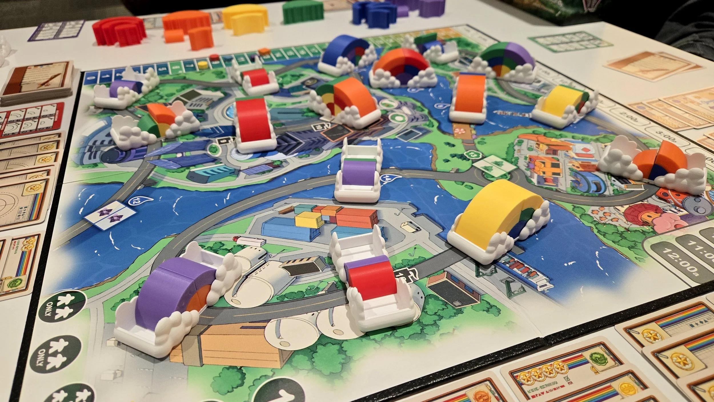 A colorful board game, called Rainbow Blvd., with rainbow and cloud-themed pieces on a game board depicting a waterway and various landscapes.