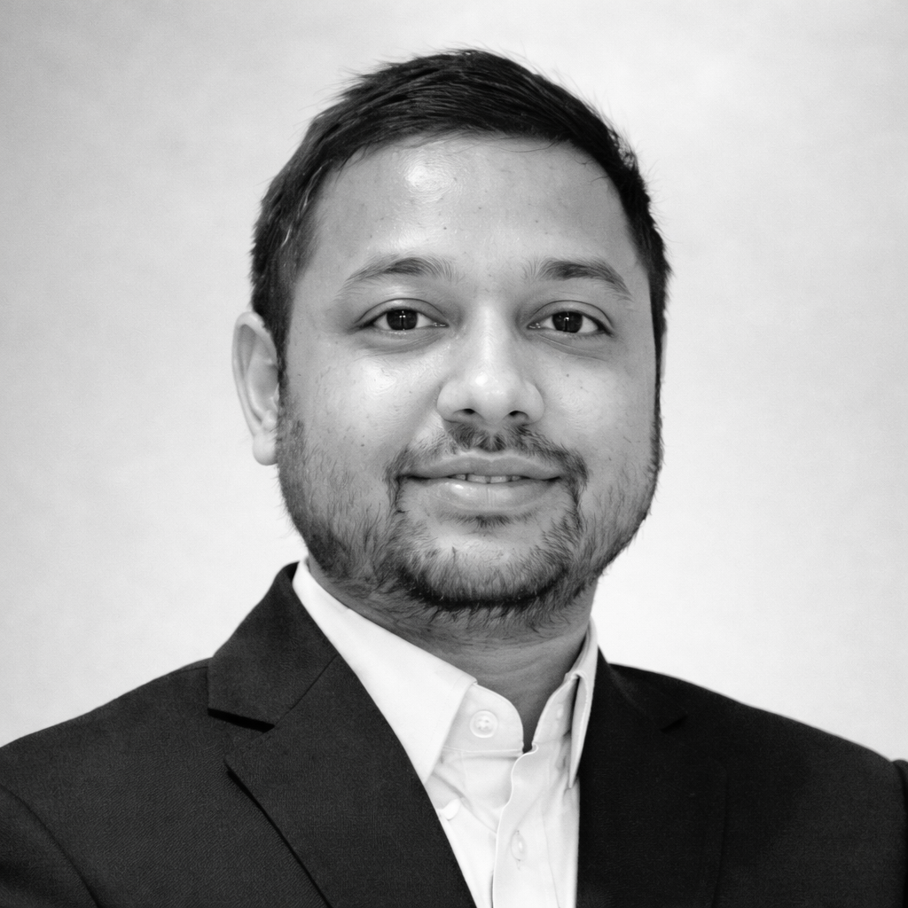 Black and white portrait of a young man with short hair and a beard, wearing a suit and collared shirt, smiling slightly.