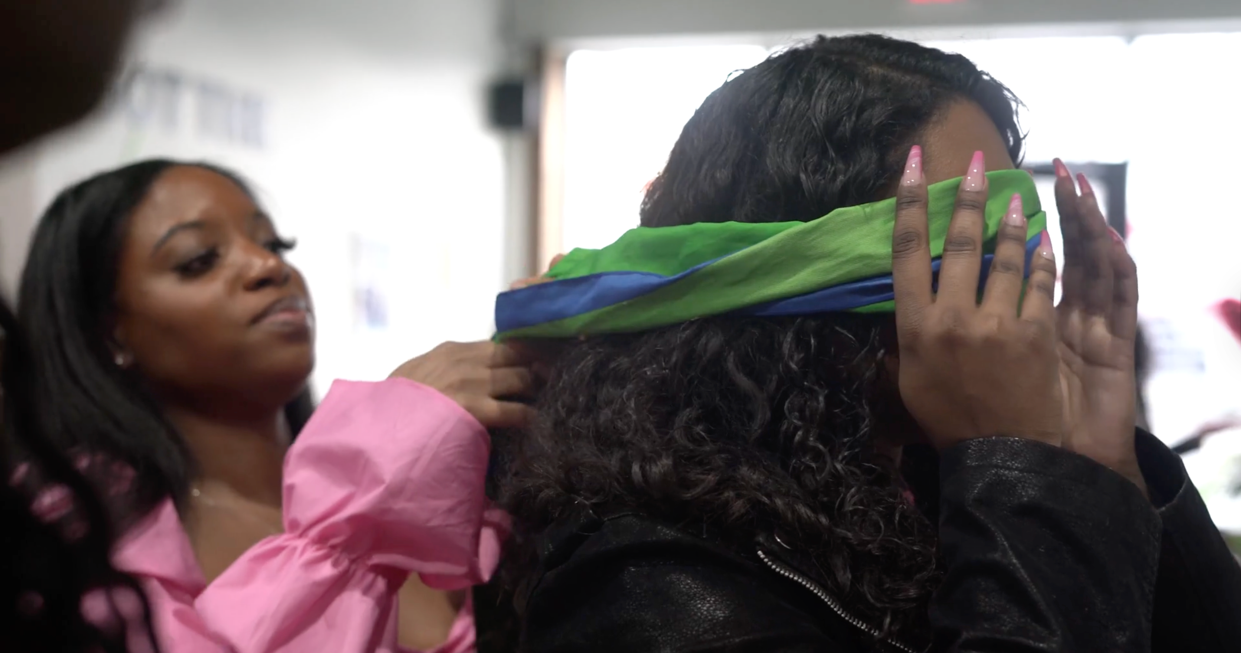 A woman in a pink shirt is blinding another woman in what appears to be a game at a social.