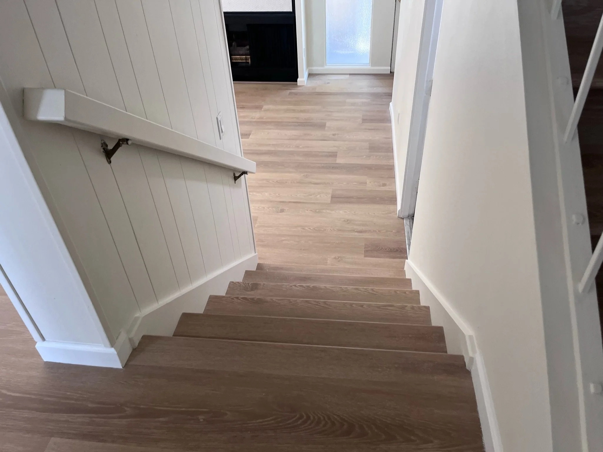 Indoor staircase with wooden steps and white walls, leading to a hallway with a light wood floor and a door with frosted glass.
