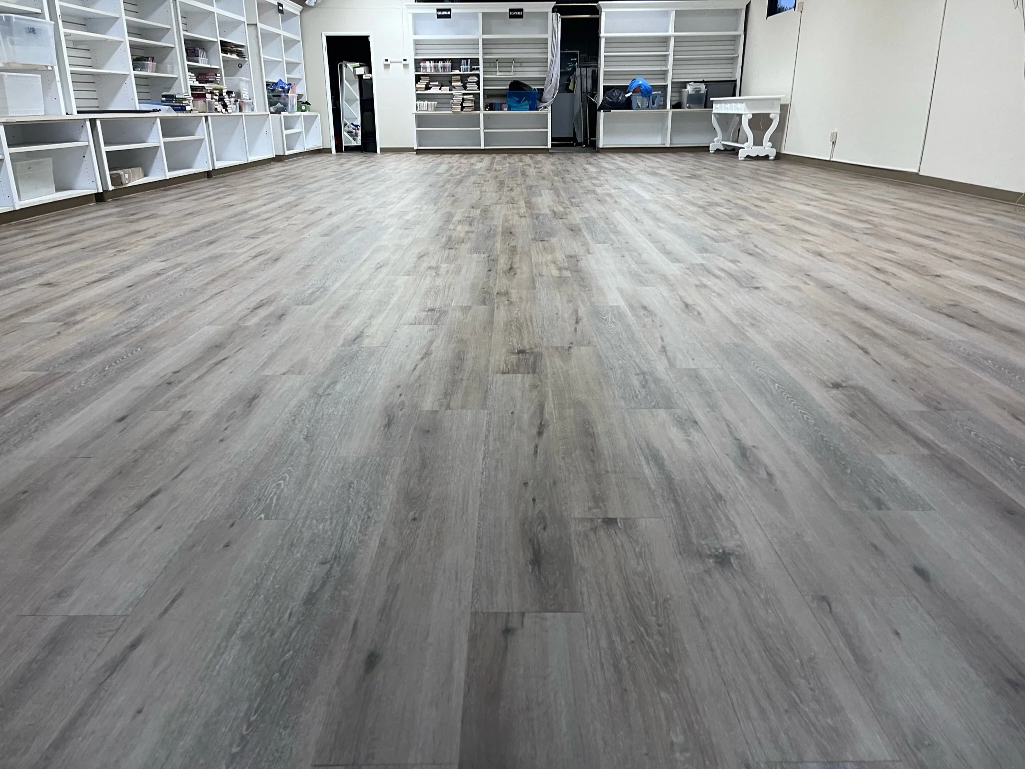 Empty room with wood-look flooring, white shelving on the wall, and a small white table in the corner.