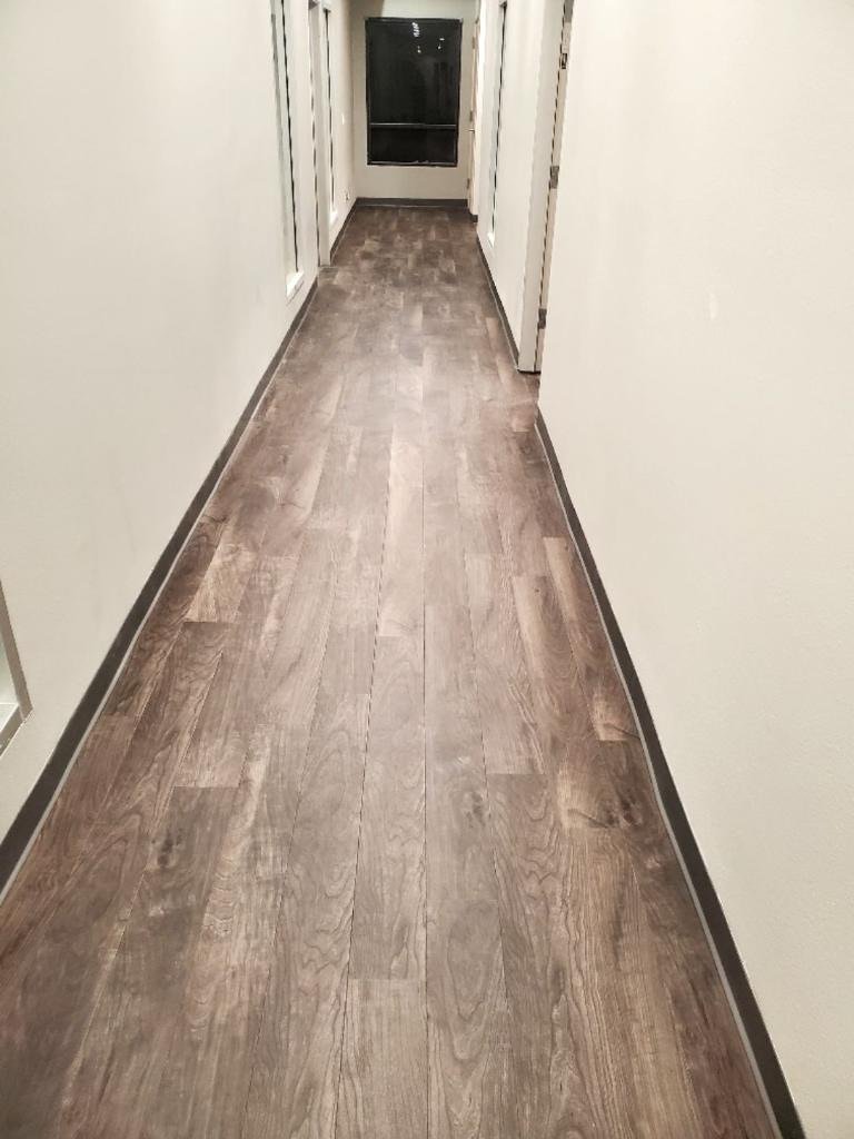 Empty hallway with wood flooring and white walls, leading to a door with a dark window at the end.