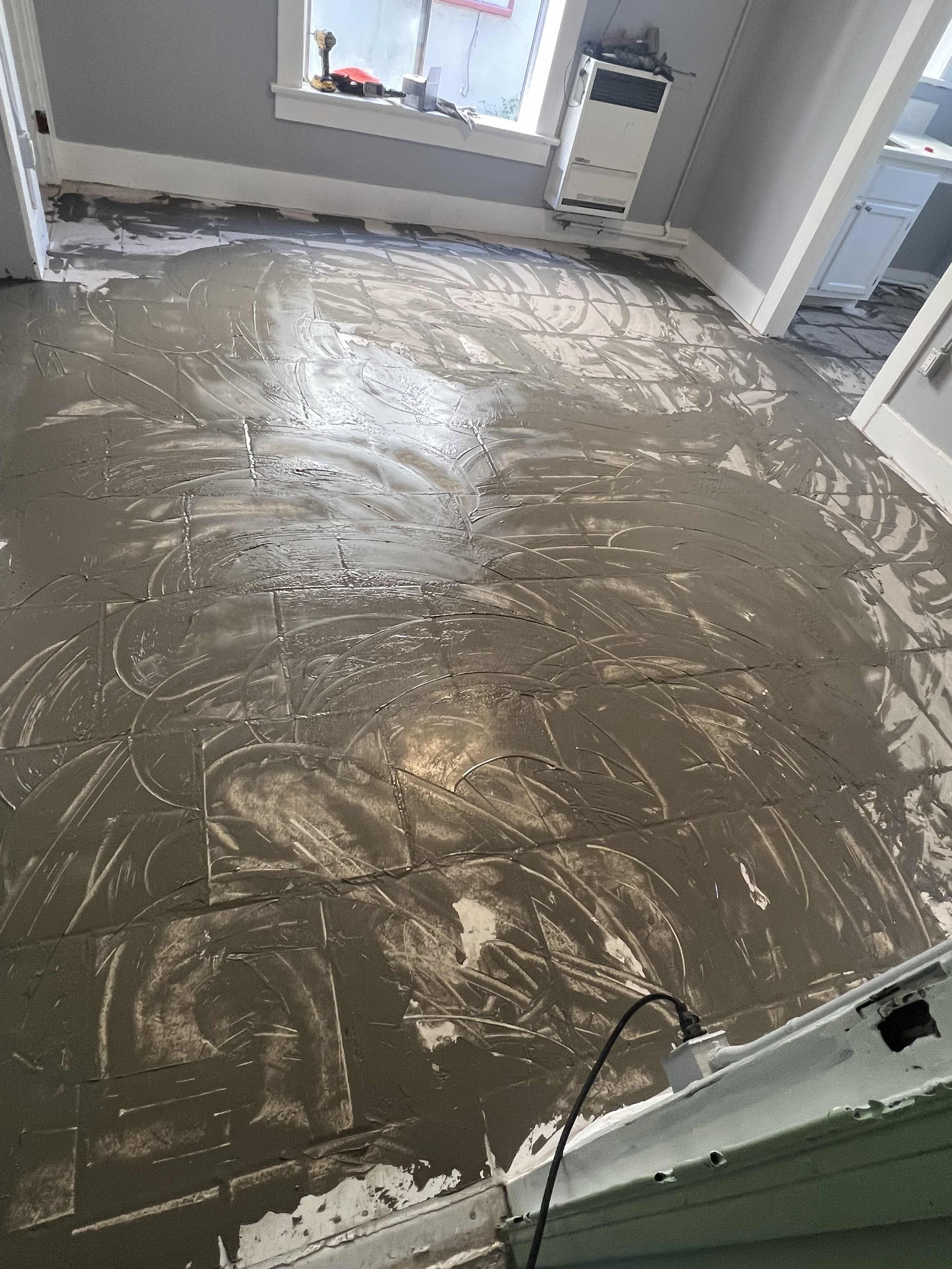 Interior room with a freshly poured concrete floor, partially smoothed out with swirls and trowel marks, near a window and doorway.