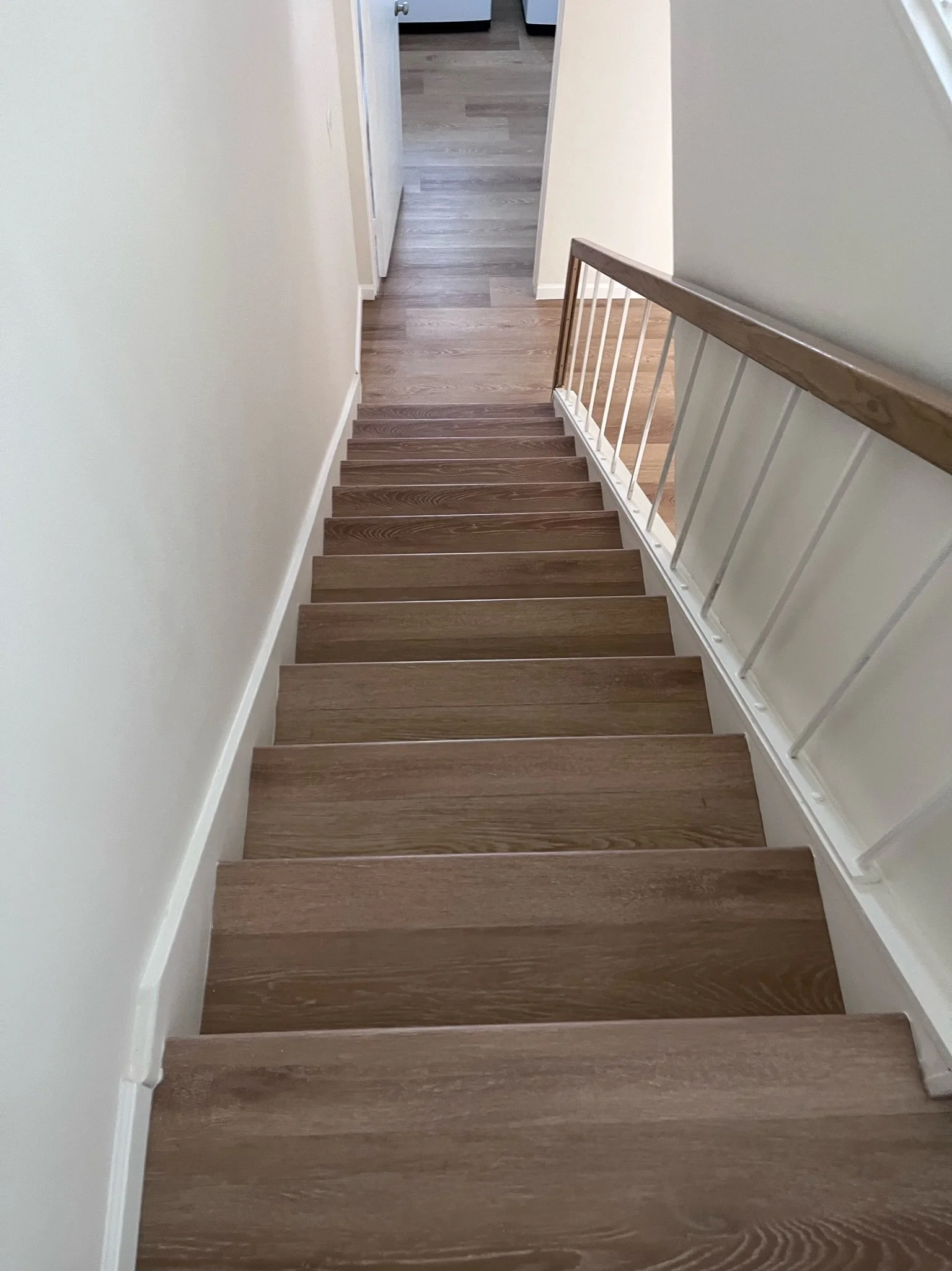 Top of a staircase with wooden steps and white railings, view looking down from the top.