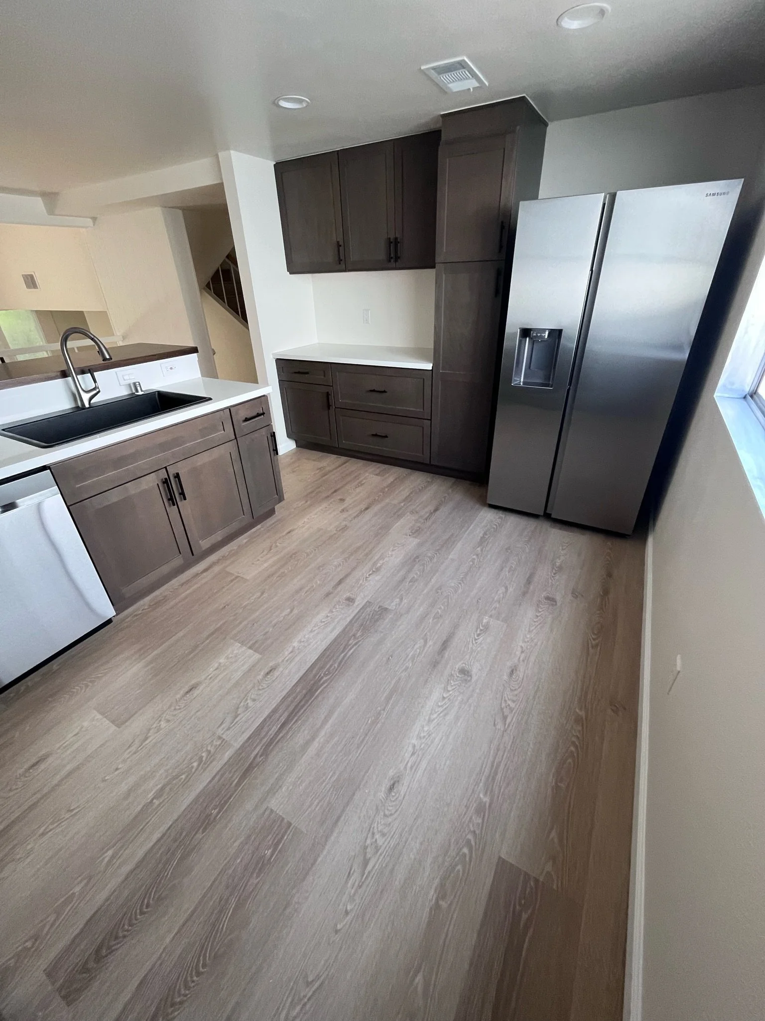 Kitchen with wooden cabinets, stainless steel refrigerator, and a white countertop with a room visible through a pass-through window.