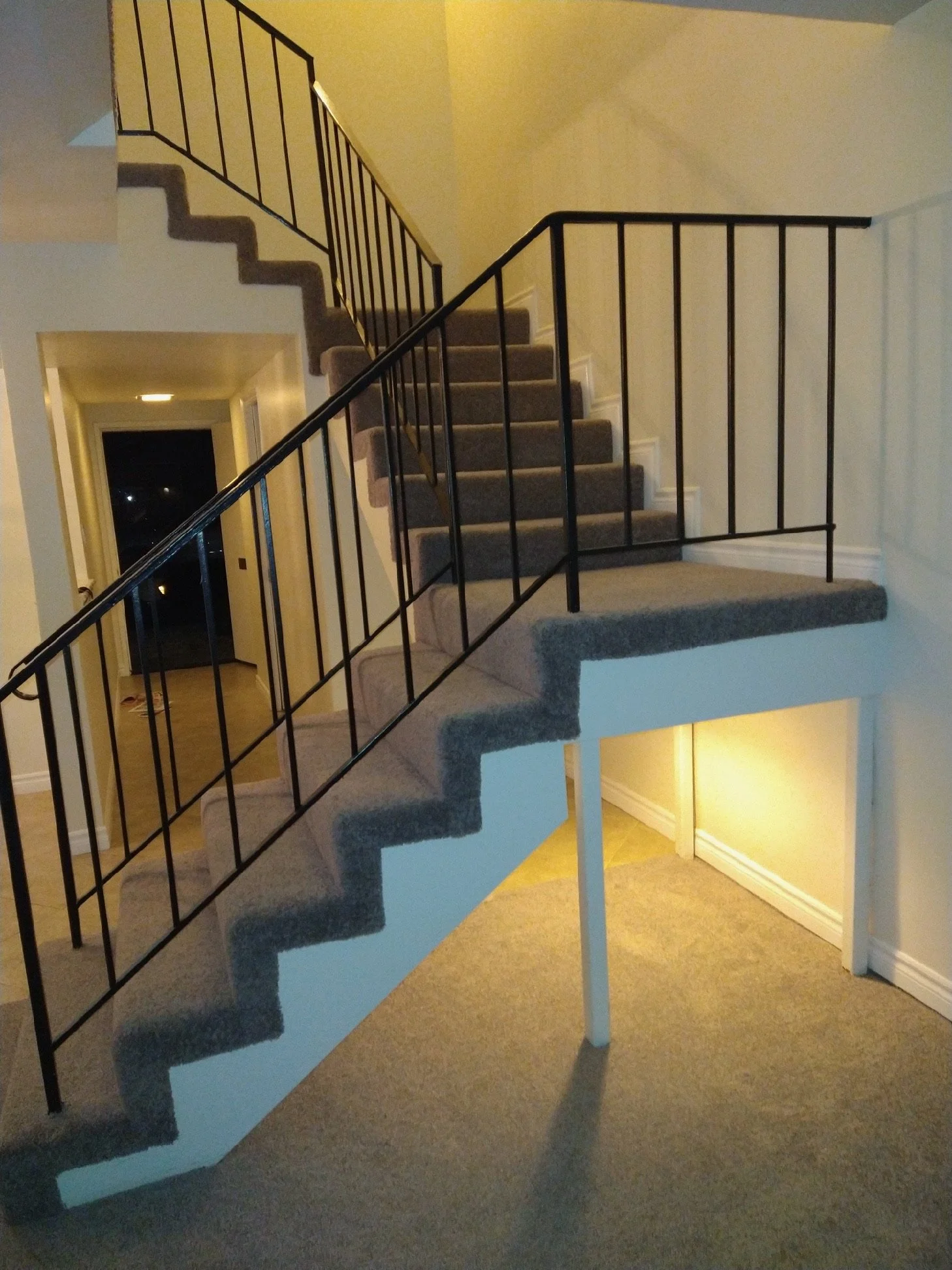 Inside view of a staircase with carpeted steps and a black metal railing, leading to an upper floor and a lower level.