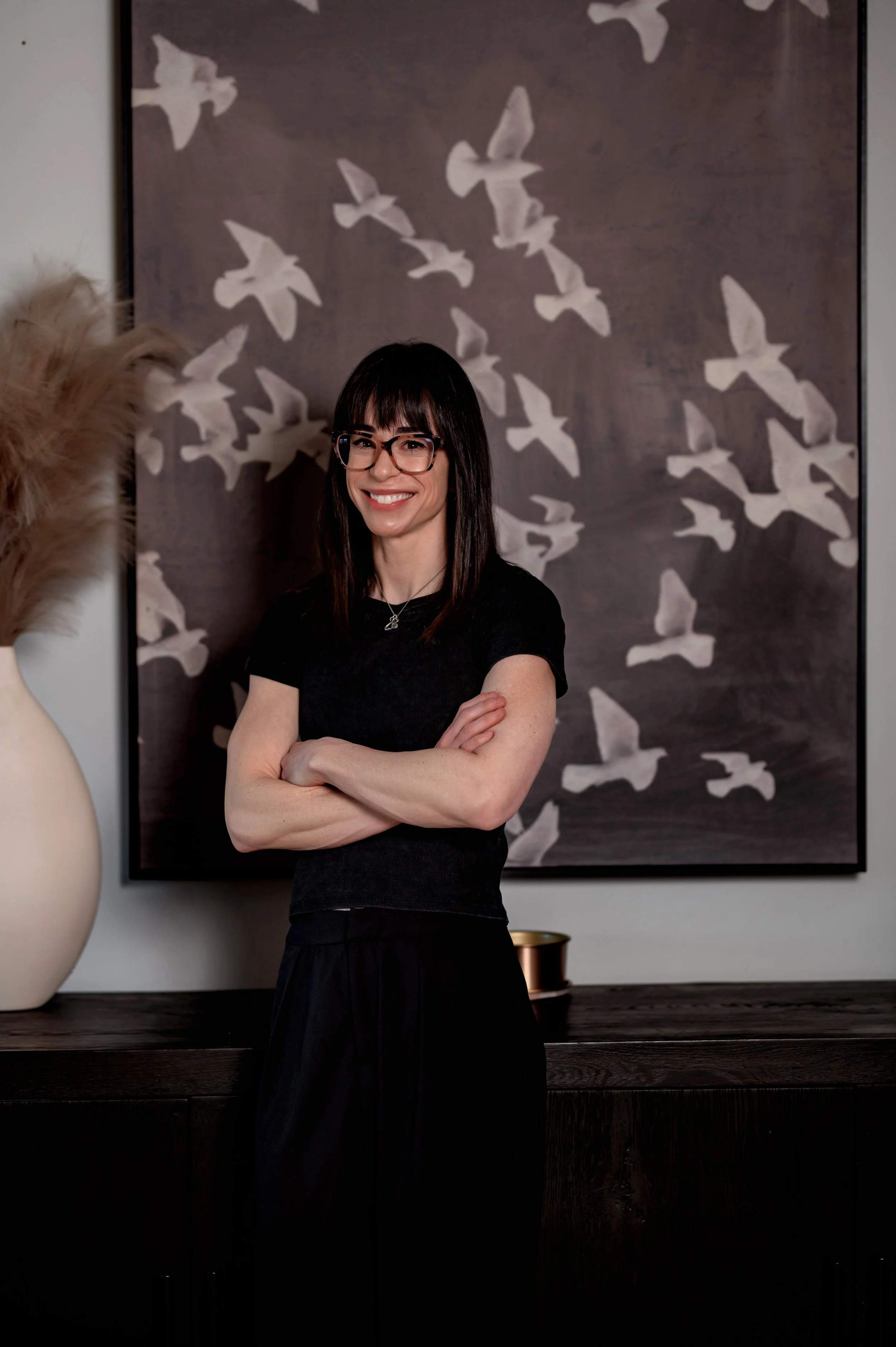 A woman with glasses and a camouflage shirt talking to a female athlete with a bun hairstyle at a sports event, with a man standing nearby and others in the background.