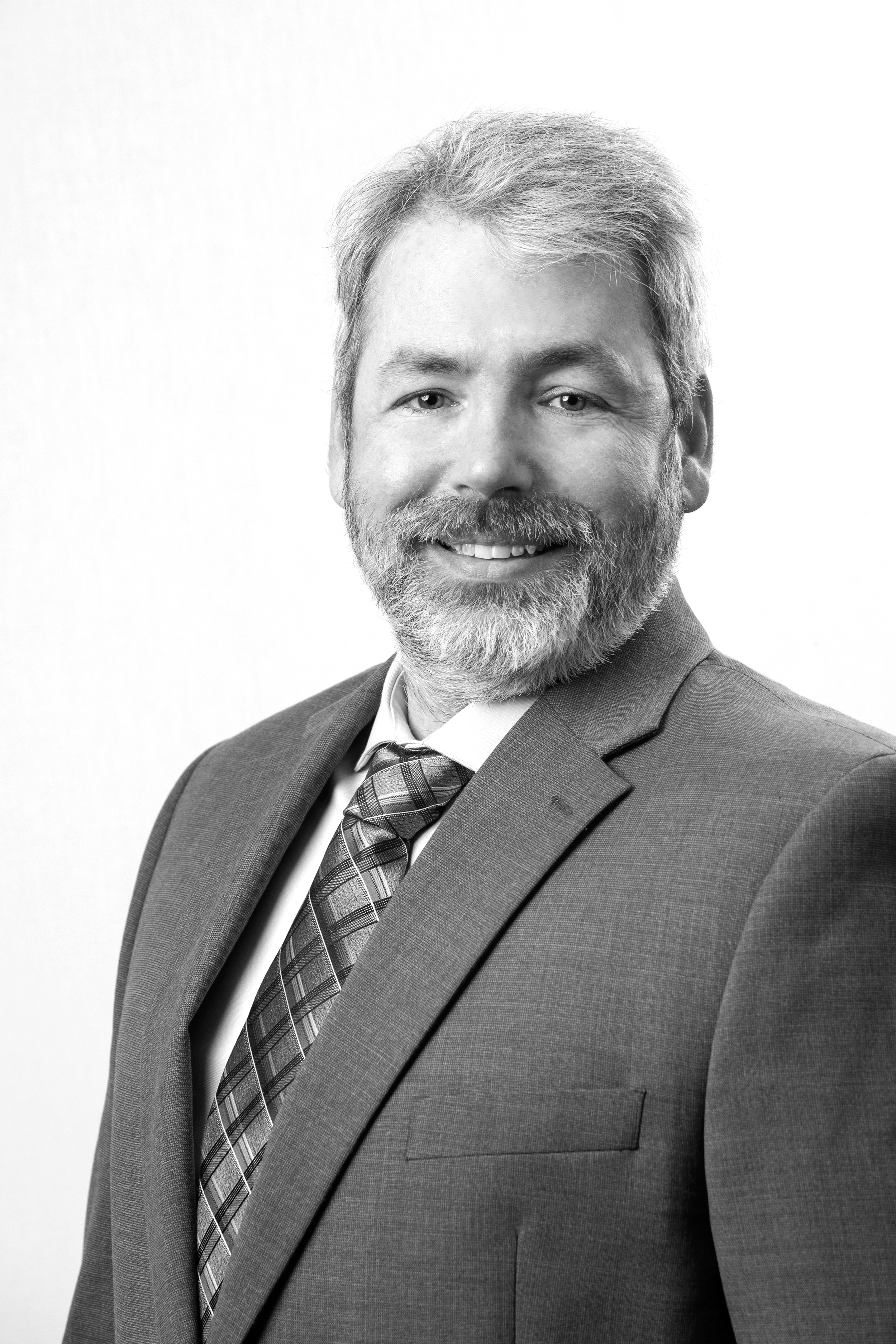 Black and white professional headshot of a smiling man with a goatee, wearing a suit jacket and a collared shirt, against a plain white background.