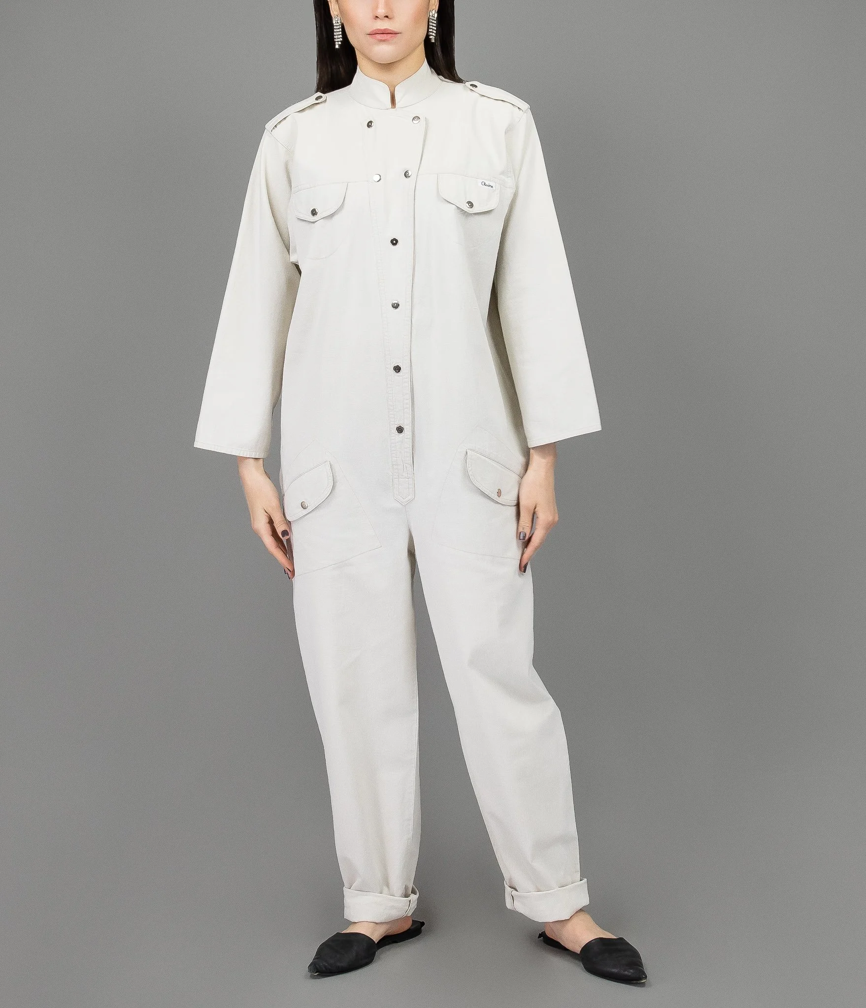 collector of vision model is wearing a size large white casual jumpsuit with mandarin collar, snap closure, long sleeves, bust and hip pockets, styled with black leather flats, and crystal earrings