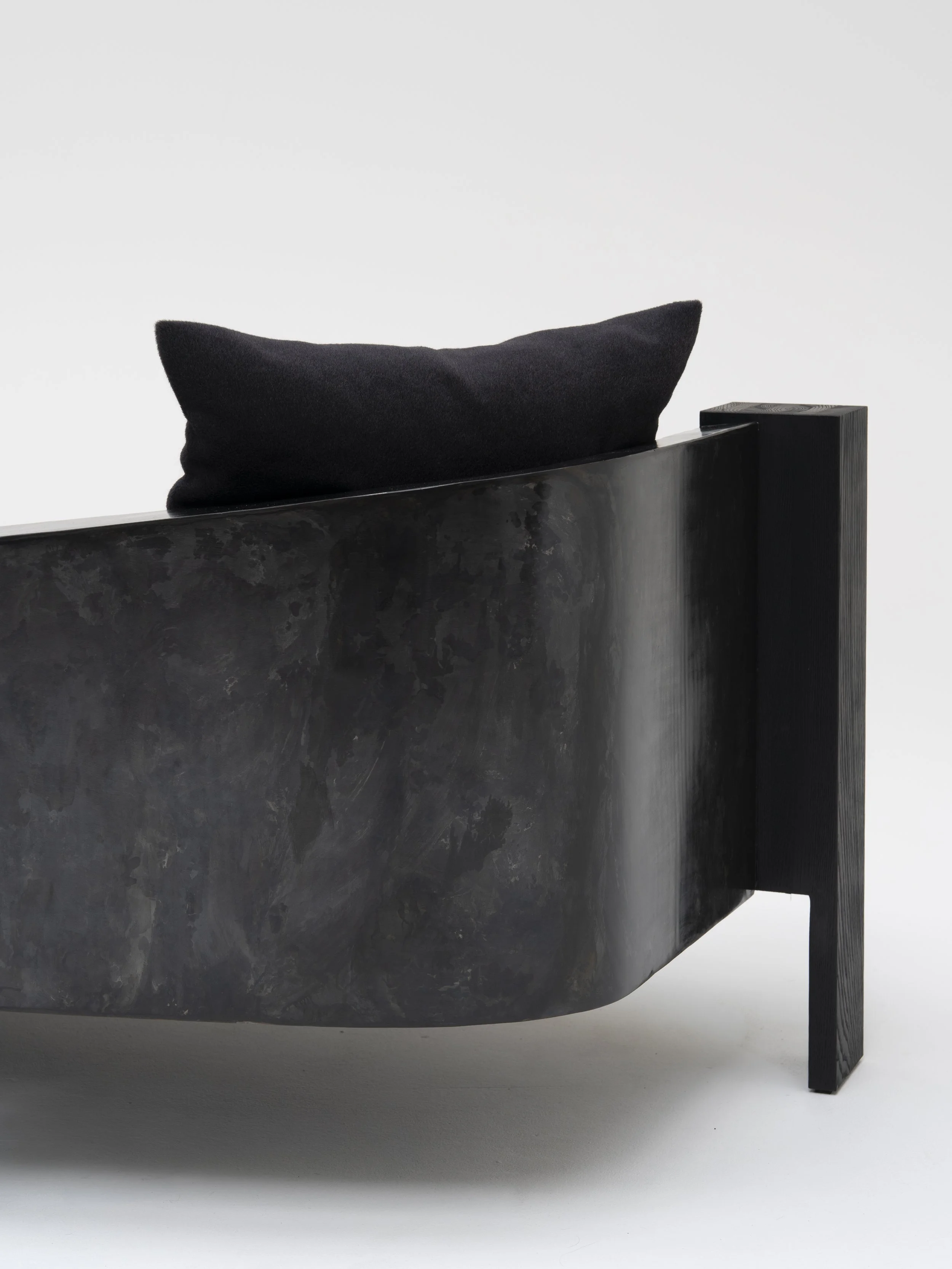 Rear detail of a black curved armchair with a textured back, angular supports and a loose cushion.