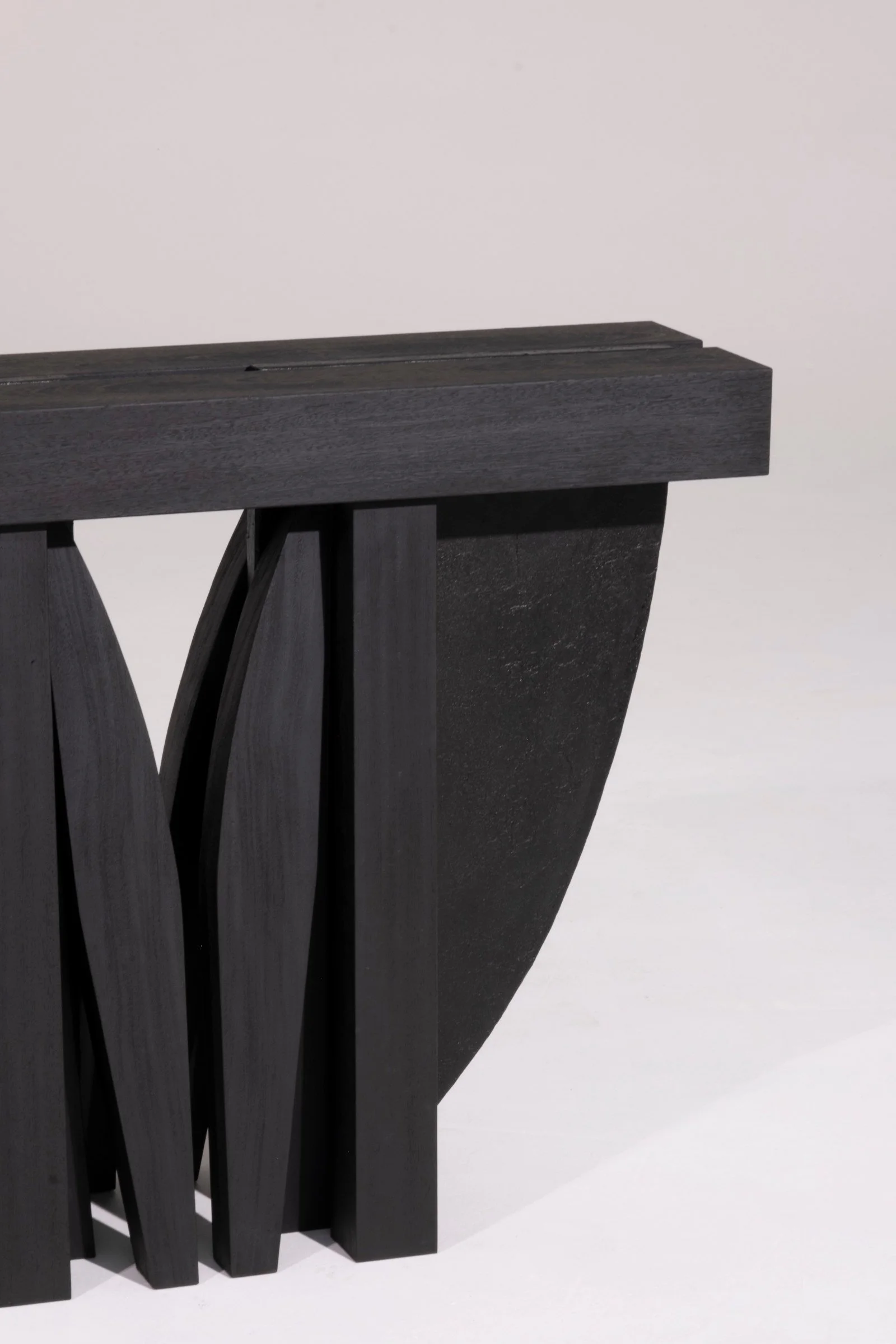 Detail of the curved burned Iroko and steel base of the Umbo Hallway Table by Arno Declercq.