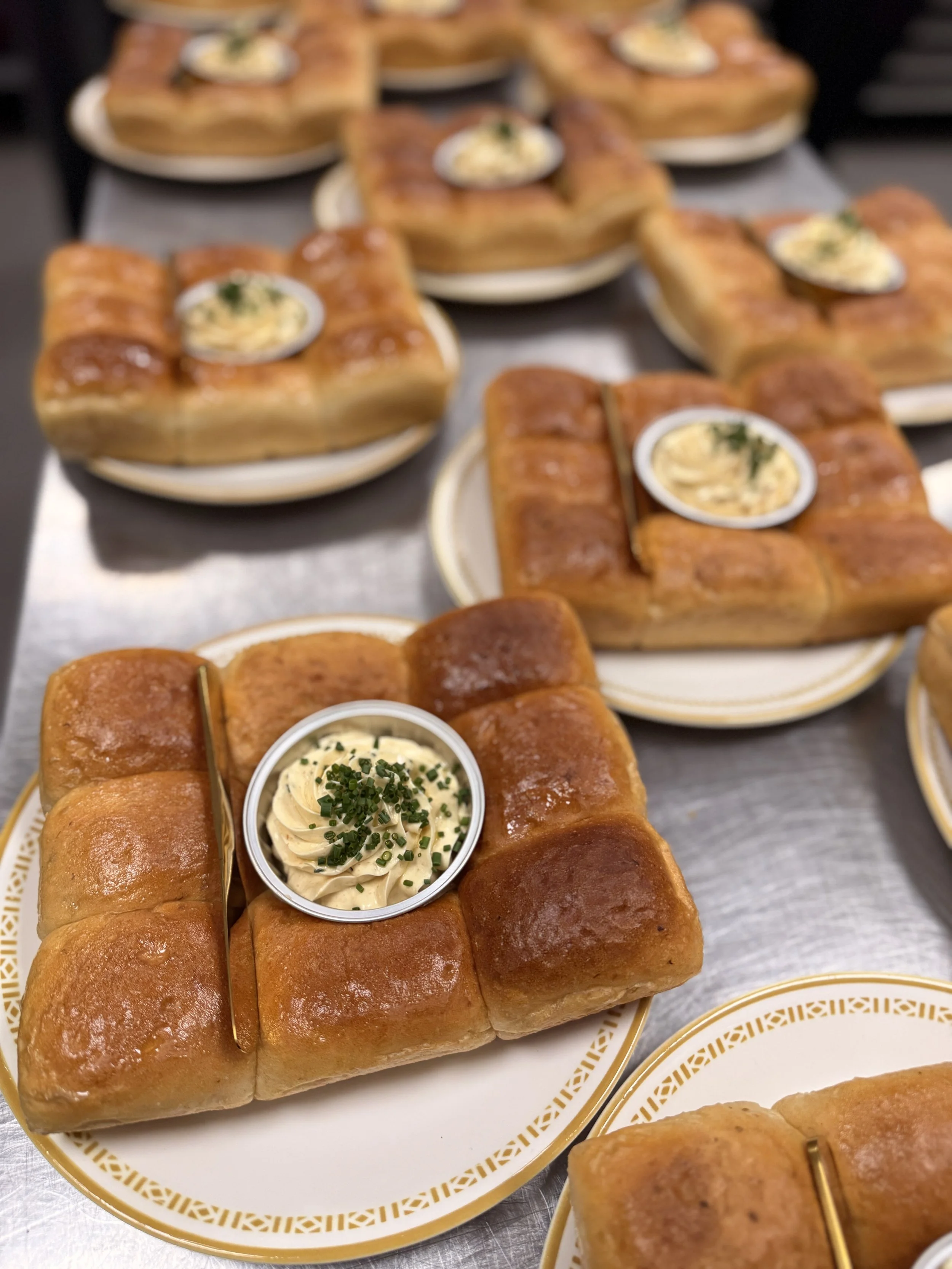  Plates of baked bread rolls filled with creamy spread and garnished with herbs, served with small cups of additional spread on top.
