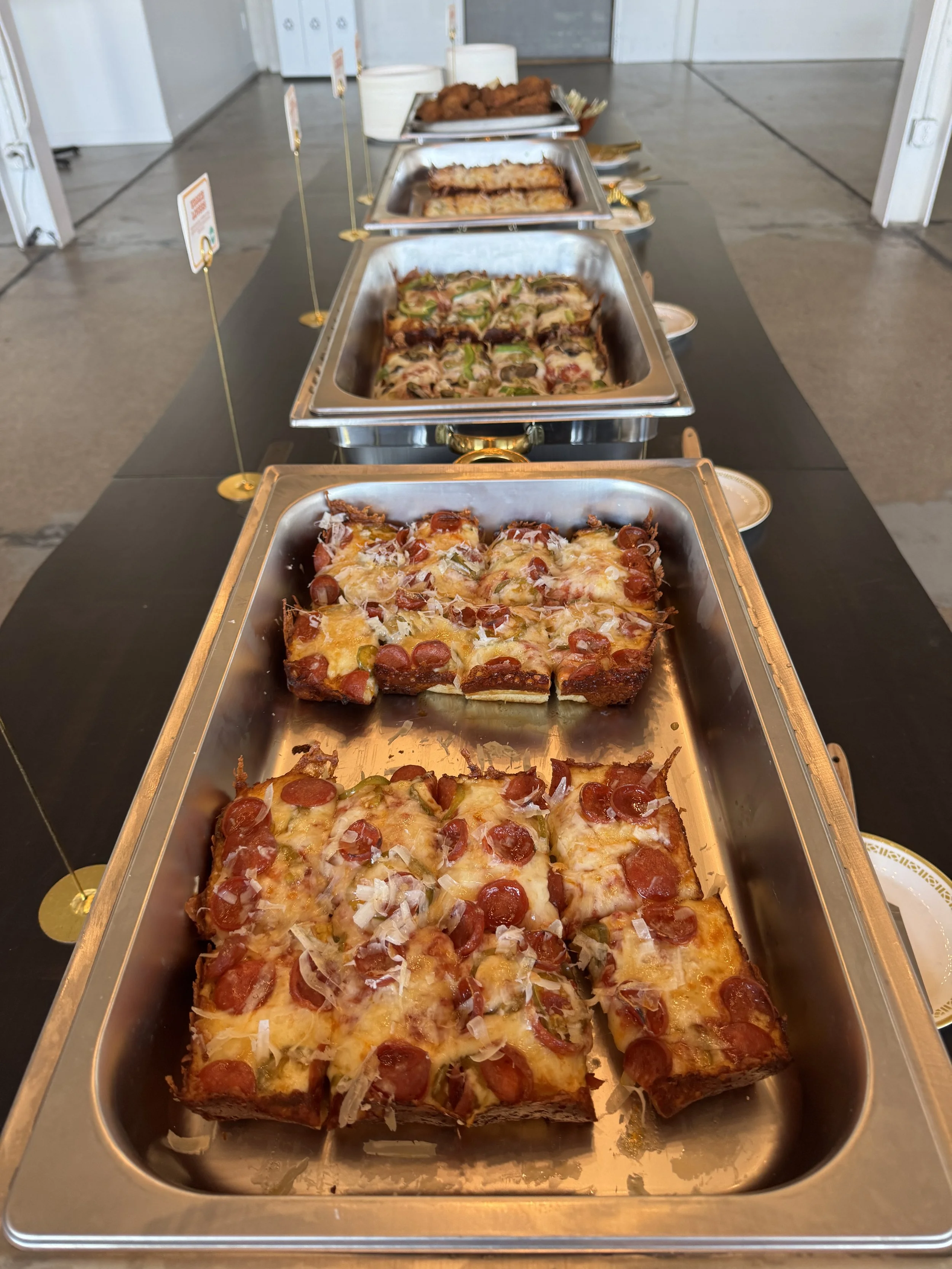 Buffet tray of assorted pizzas with toppings such as pepperoni, sausage, and vegetables in a catering setup.