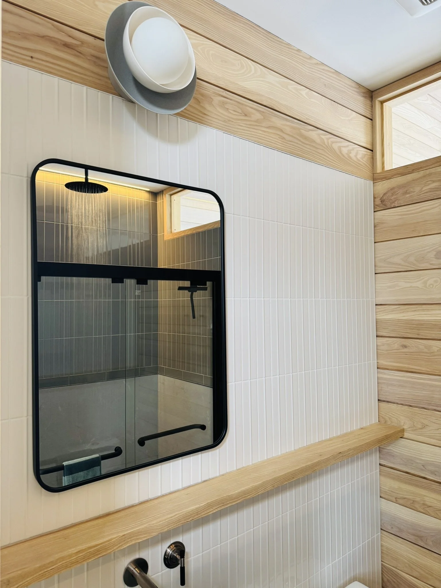 Accessible bathroom at Hinterhaus 41 by Elevin Design Studio featuring ash tongue and groove walls, white Scandinavian tile, a transom window, and a rounded black mirror, contemporary residential interior, photo by Brad and Shawn Hernden