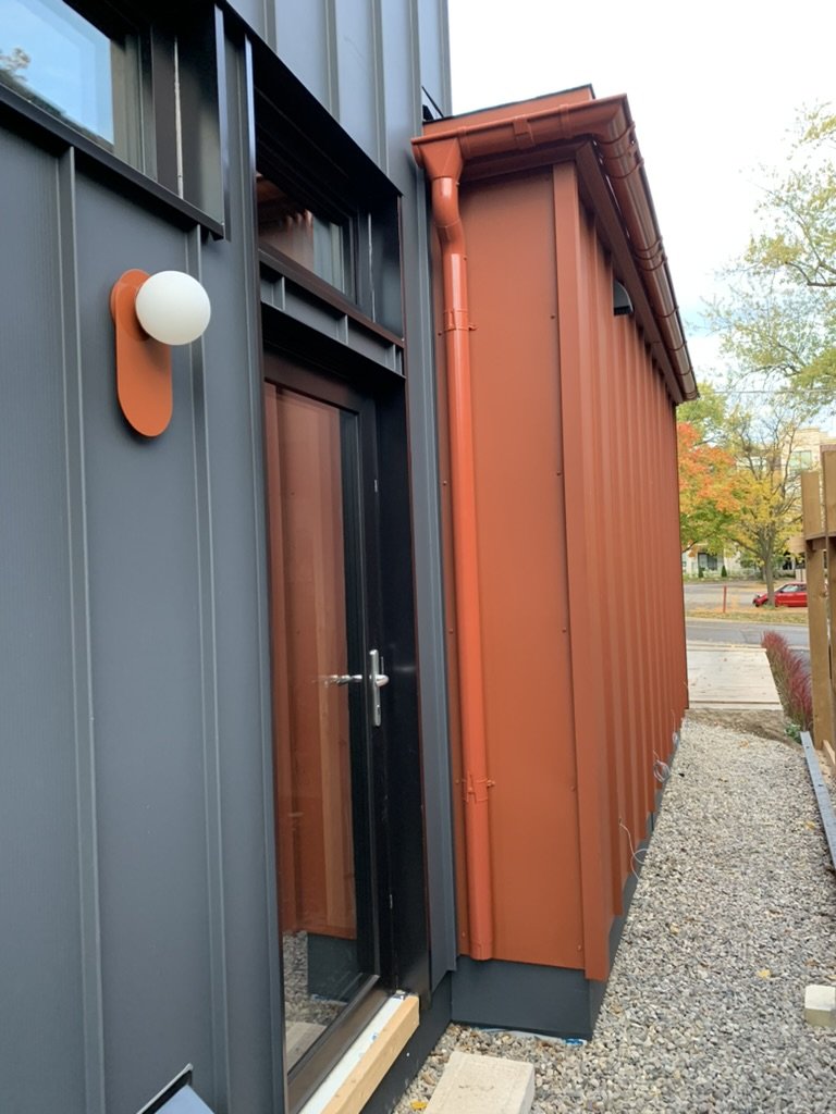 Rust and charcoal standing seam steel façade with half-round eaves by Ruukki at Hinterhaus 41 by Elevin Design Studio, featuring an Arch wall sconce by Luminaire Authentik, photo by Brad and Shawn Hernden.