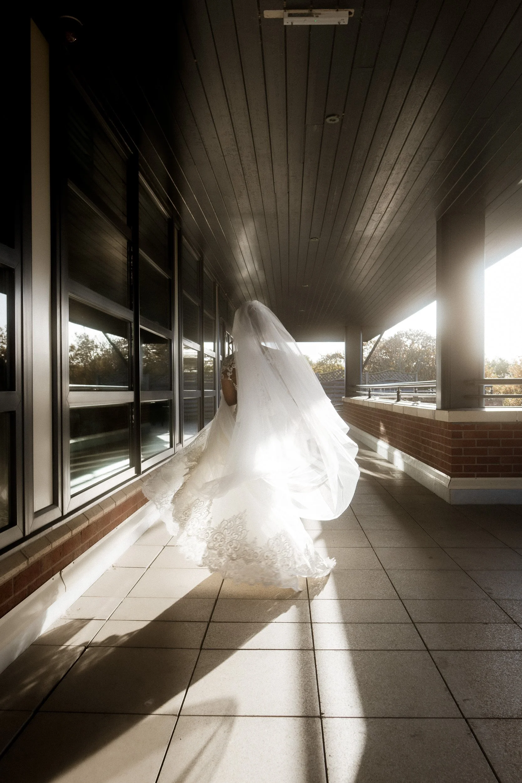 Bride walking on a balcony in her wedding dress and veil with sunlight casting shadows.