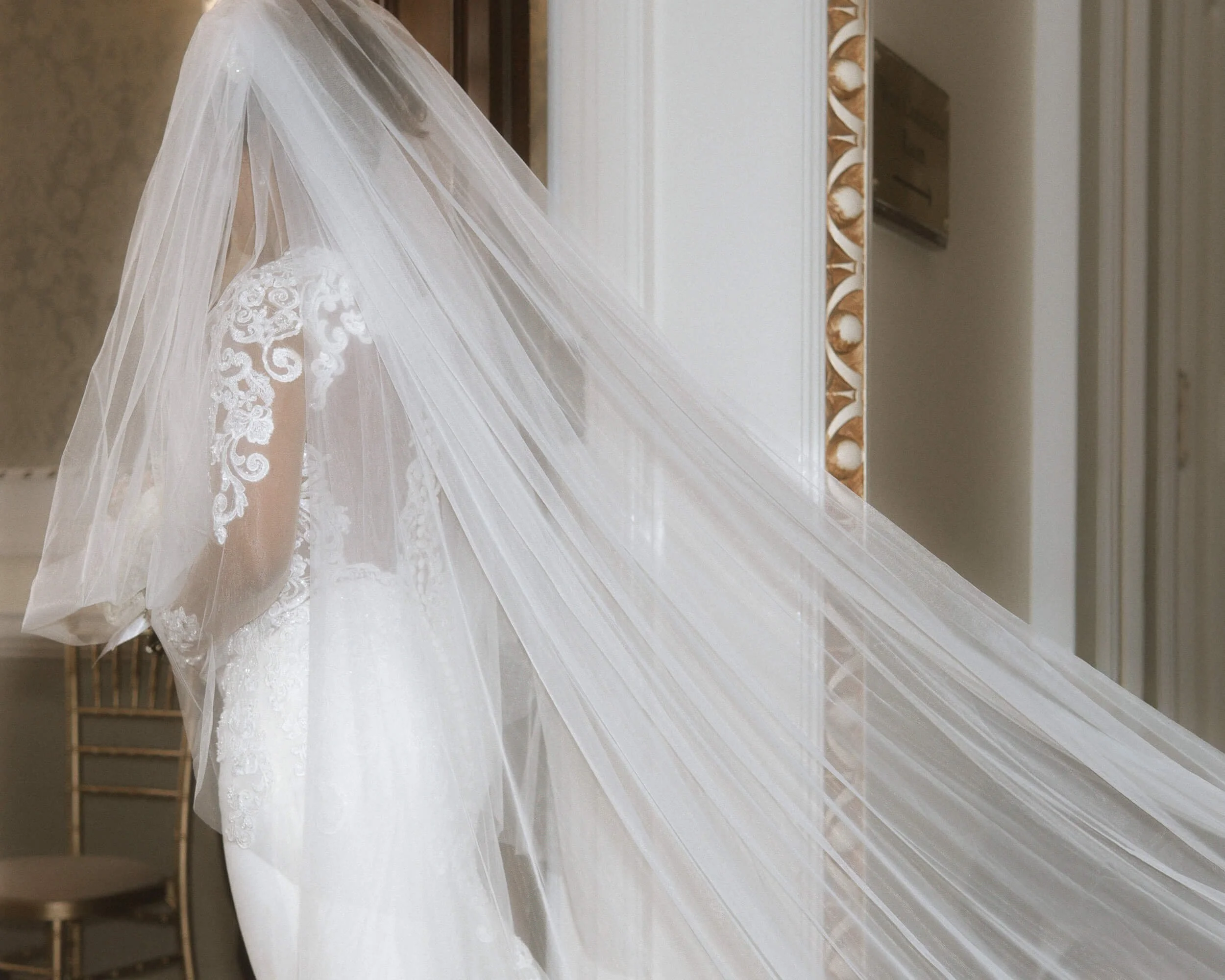 Wedding dress with lace details and a long veil displayed in a room.