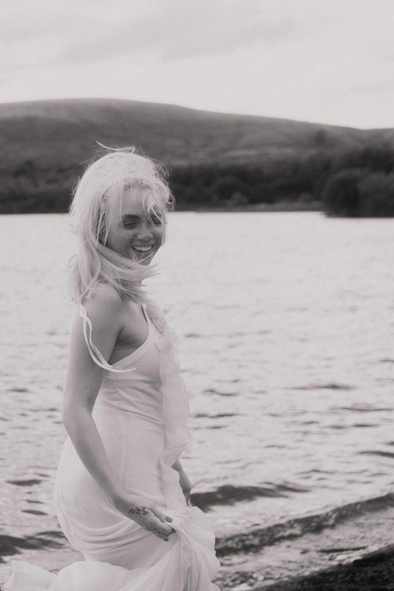 A woman standing in water, smiling, with mountains in the background, in black and white.
