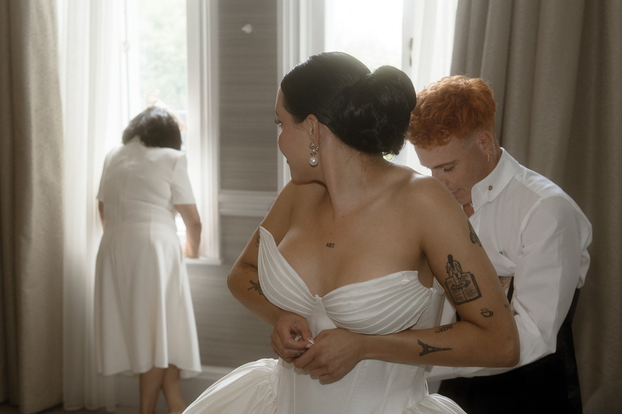 A woman in a white wedding dress is getting dressed.