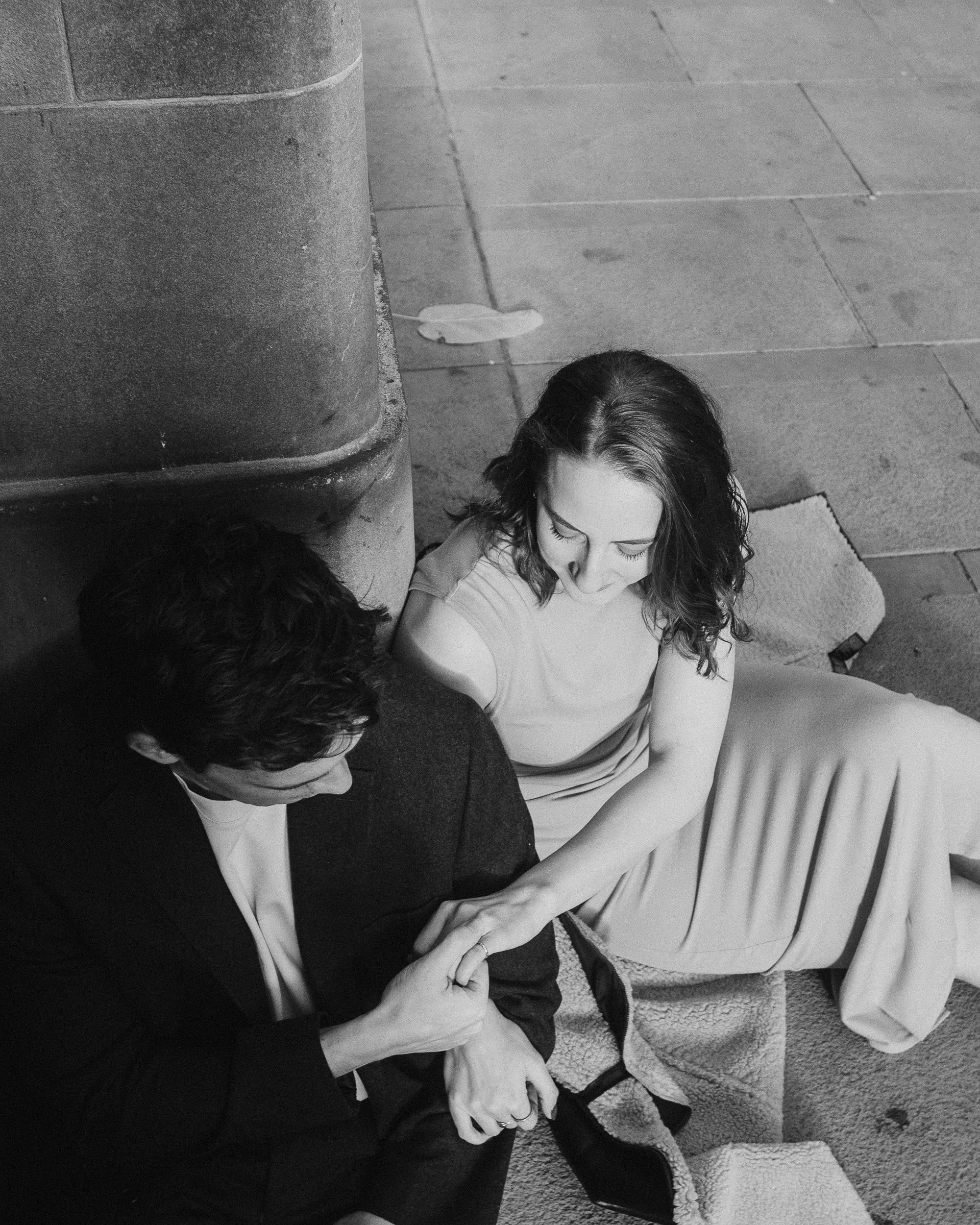 Black and white candid of a couple sitting on stone steps holding hands in a quiet moment.
