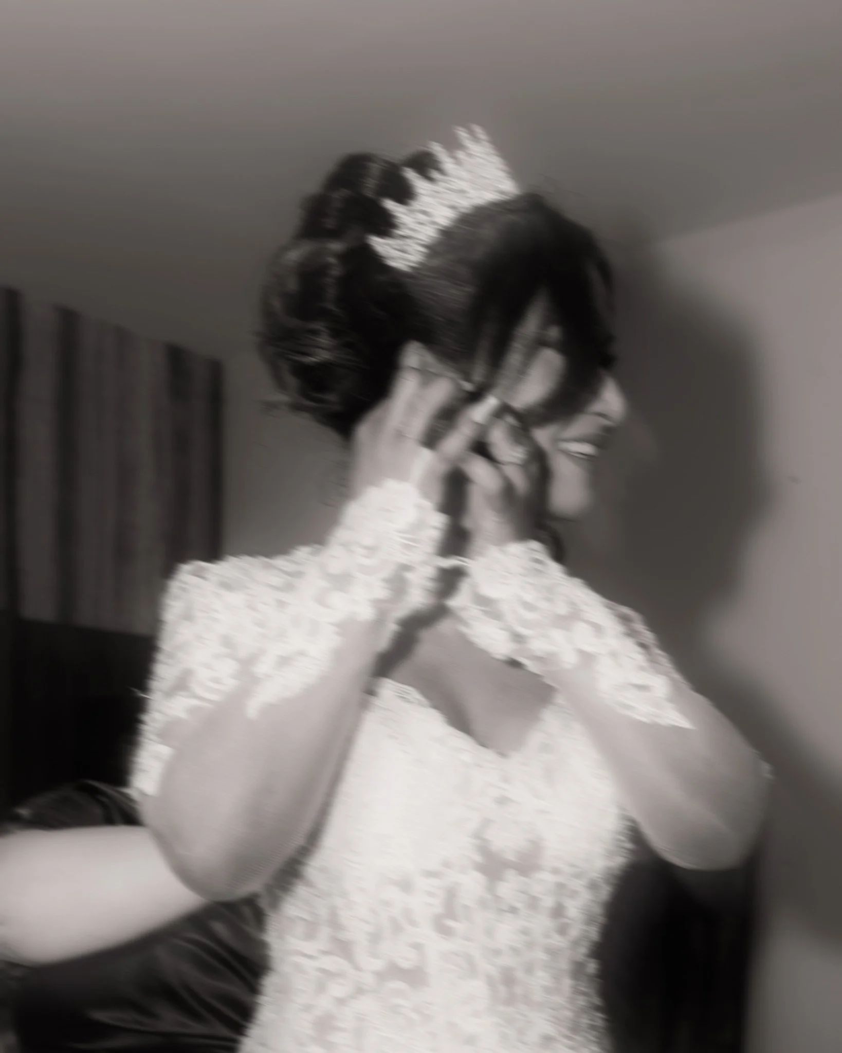 A bride in a lace wedding dress wearing a tiara and getting ready.