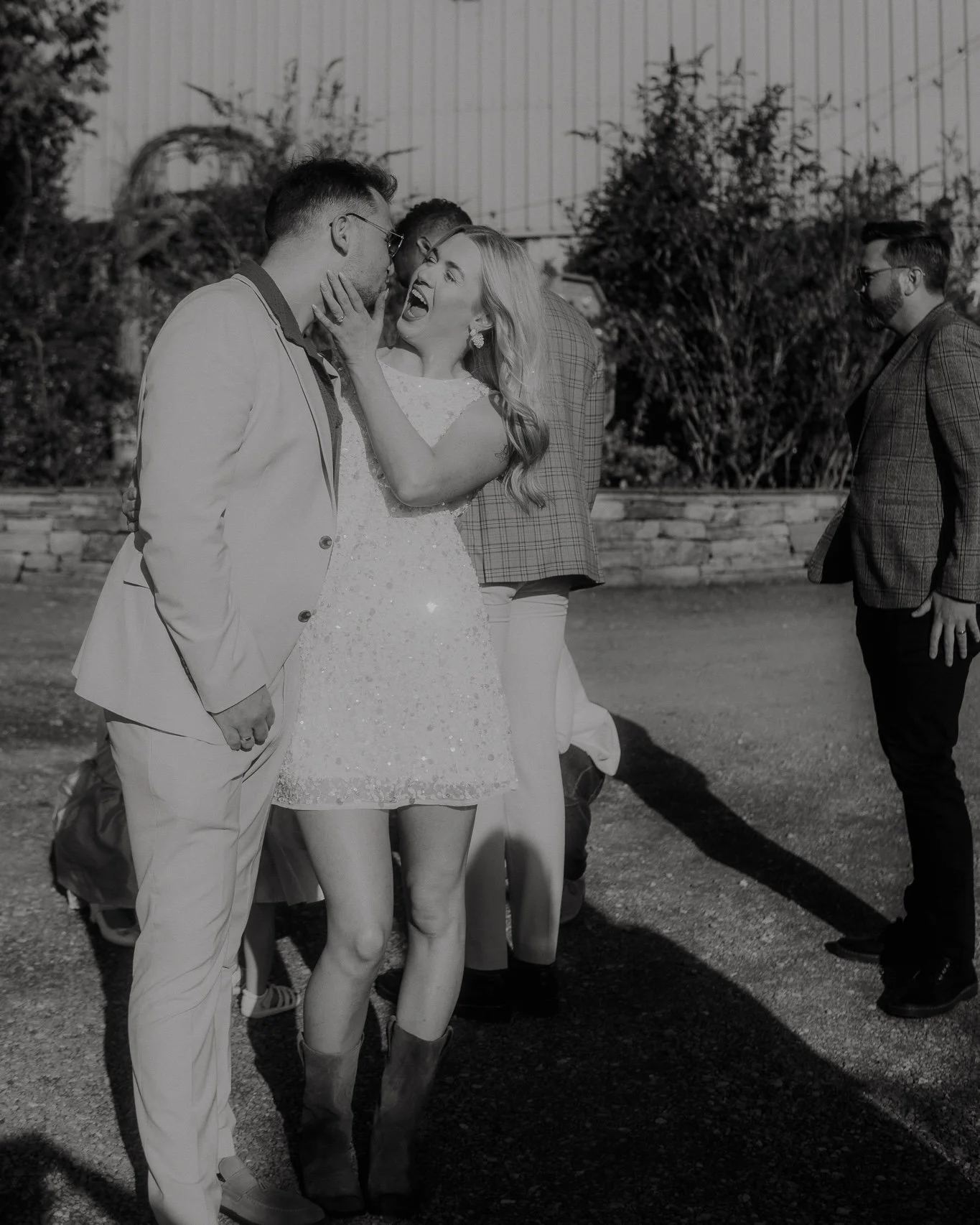 A woman in a short, sparkly dress is enthusiastically yelling at a man in a light-colored suit, touching his face, at an outdoor event.