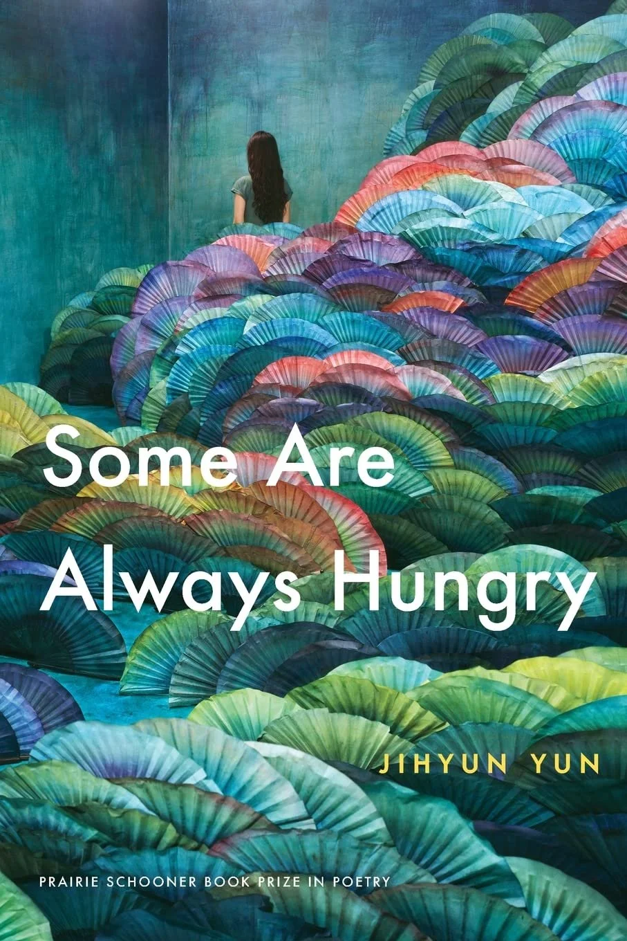 Photo of the cover of 'Some Are Always Hungry' by Jihyun Yun. The cover is a drawing filled with greens, yellows, pinks, blues, and purple-looking plants. Near the top left of the cover a person with long black hair stands with their back to the read