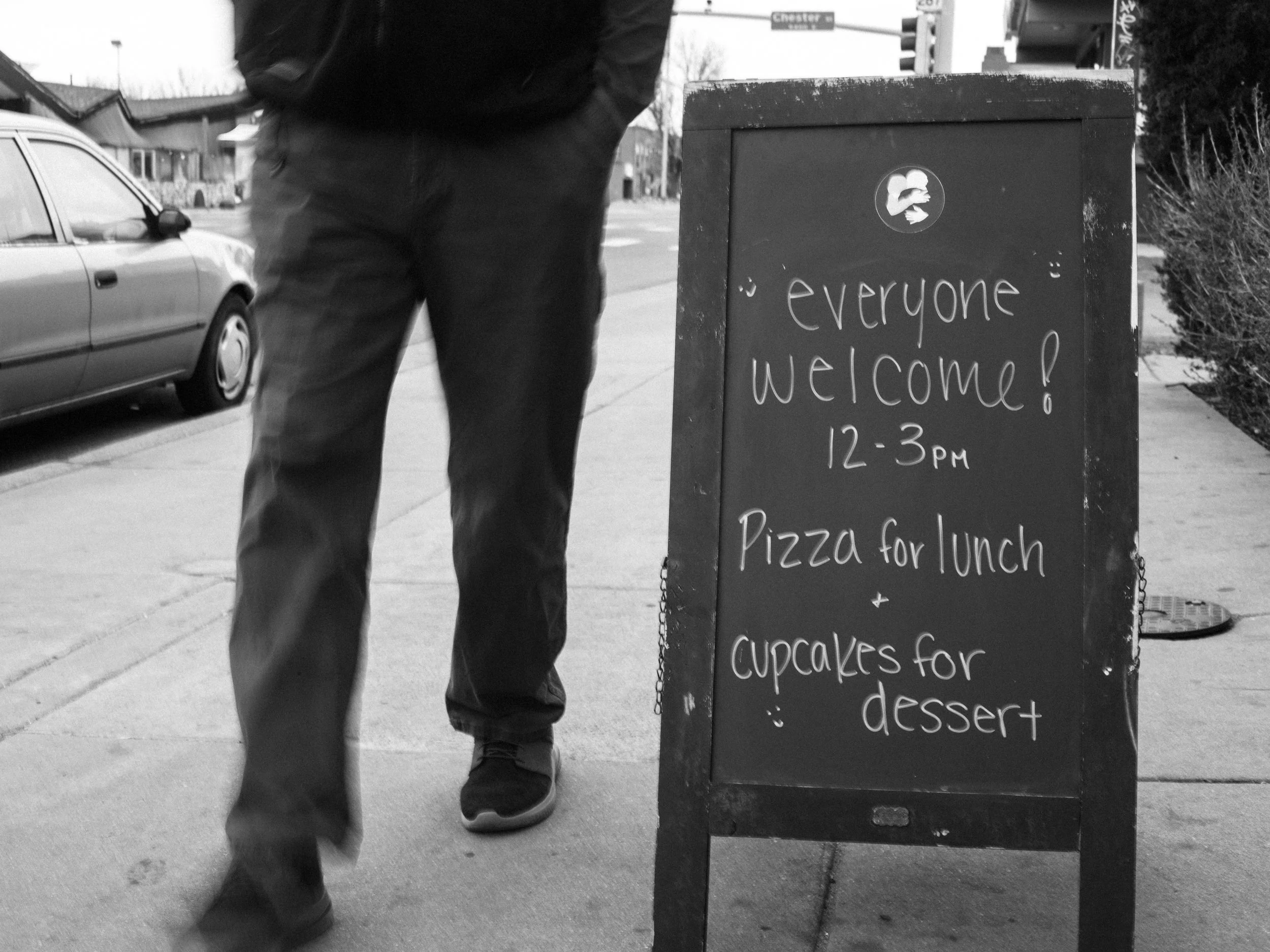 Two women conversing in a room with photos hanging on the wall; one is wearing a light-colored shirt and the other a dark jacket with a face mask, both smiling.