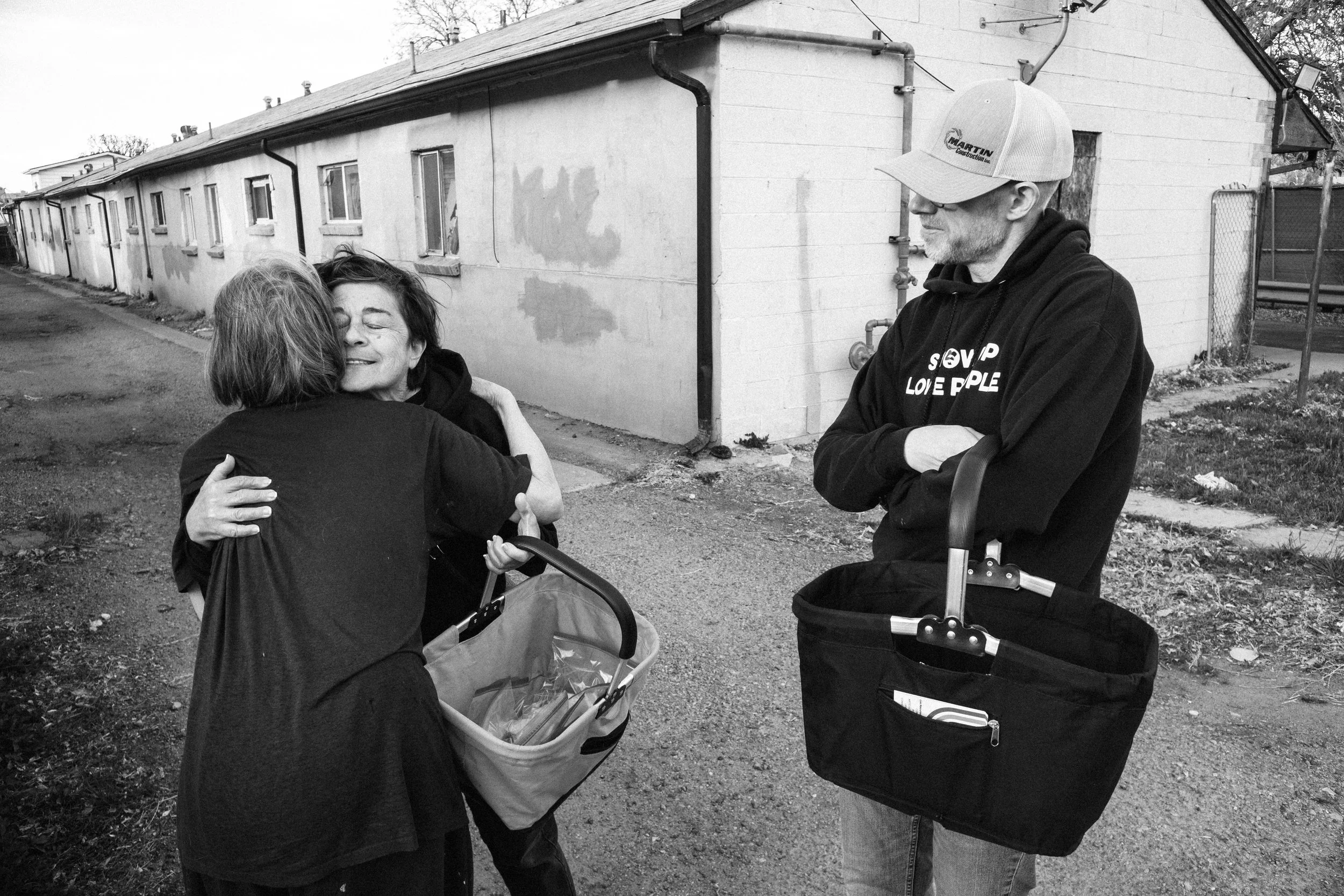 Three women in an emotional moment, two of them comforting the third, indoors in a room with hardwood floor, black and white photo.