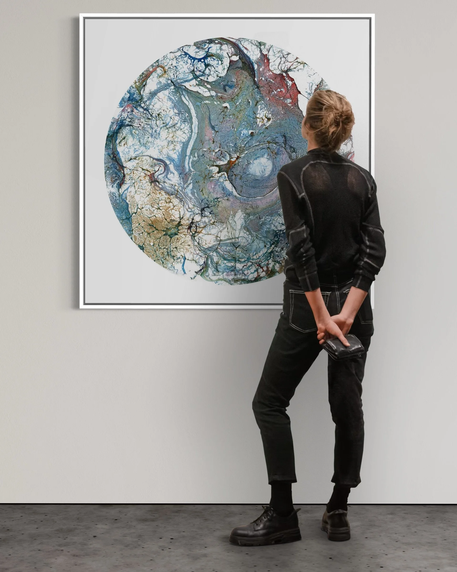 Person viewing abstract circular artwork with swirling and branching colors on a white wall in an art gallery.