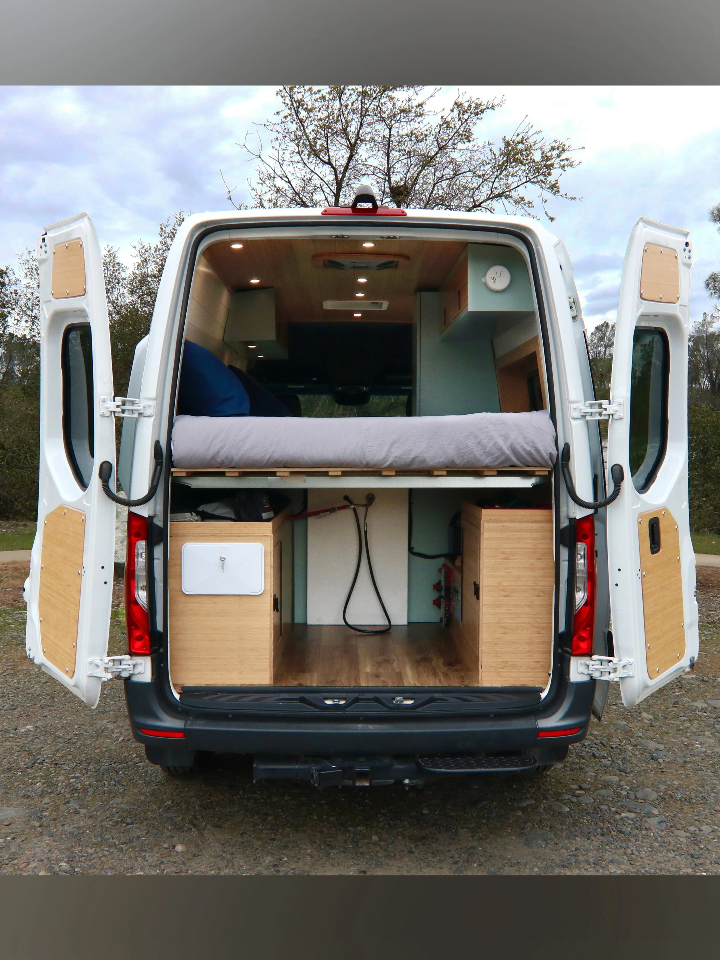 Large garage space for storage in campervan, showing outdoor shower as well. This space also houses the batteries and fresh water tank in the wheelwell boxes.