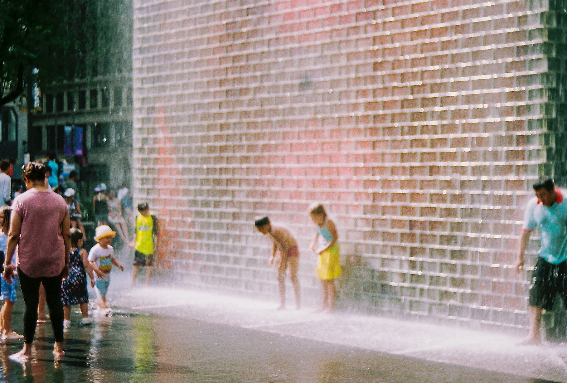 Children playing and cooling off in water spraying from a wall fountain on a city street