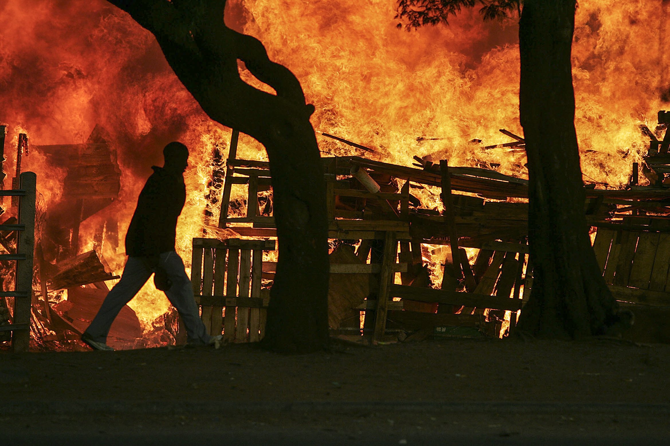 A man strides past blazing shacks set alight during fierce clashes between the police, foreigners and local residents. Makausi, Primrose, east of Johannesburg, South Africa.