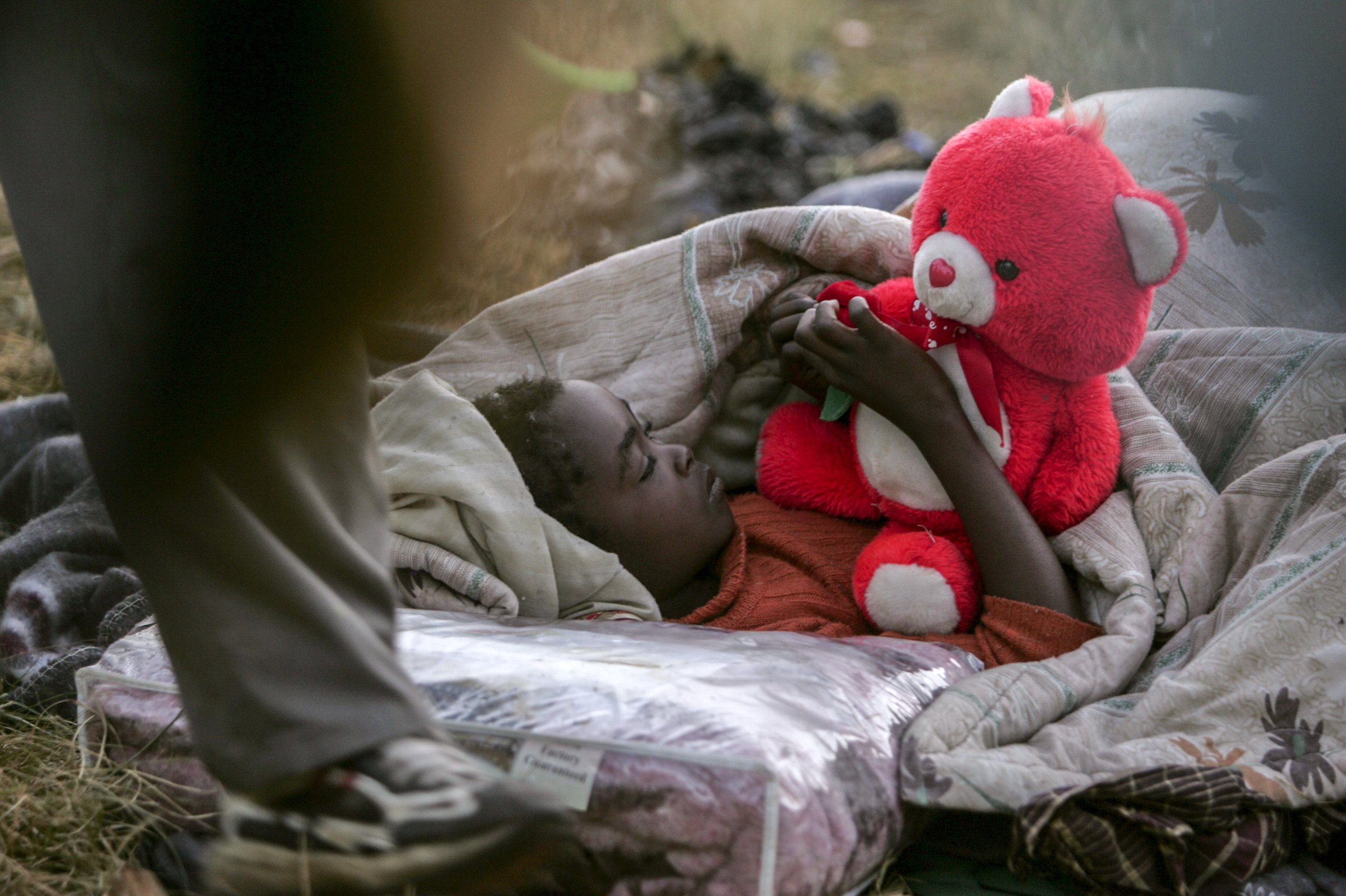 A young girl wakes up in her new home: a refugee camp opposite the Primrose police station following clashes between foreigners and local residents. Johannesburg, South Africa.