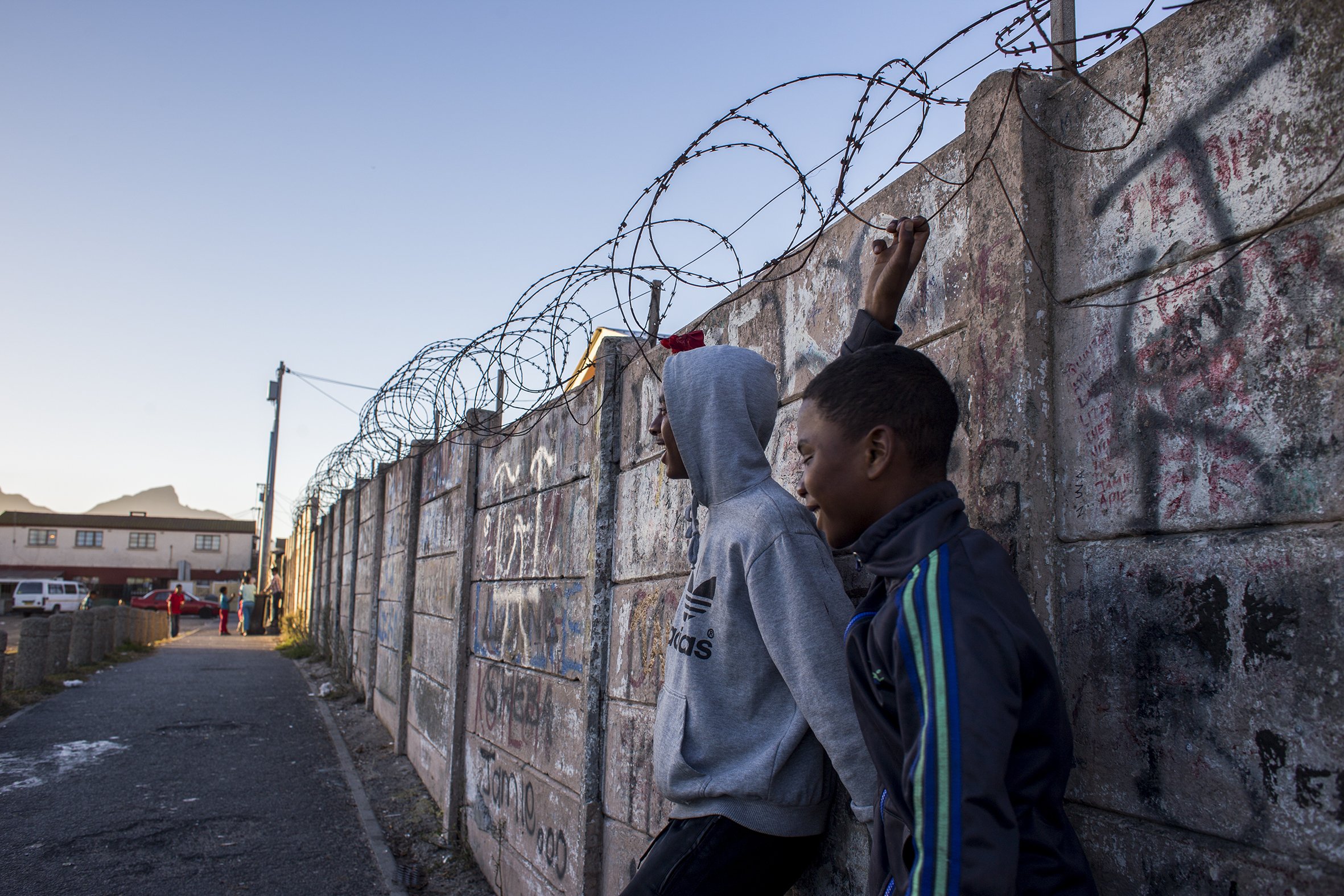 Two boys lean against a wall covered in graffiti in Parkwood, a suburb on the Cape Flats. April 2017.