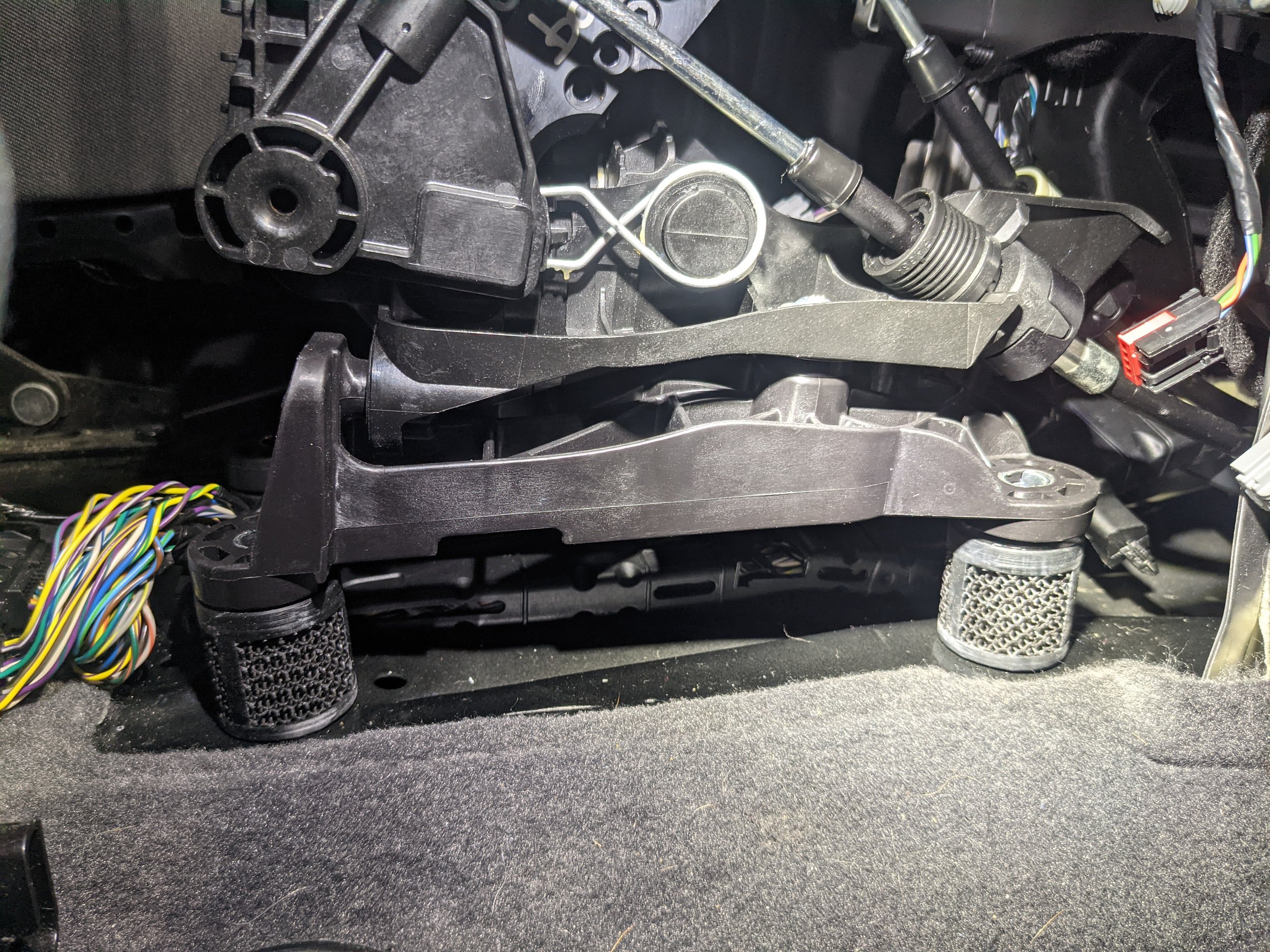 Close-up of a vehicle's interior showing the steering column assembly and wiring, with the plastic cover removed to expose mechanical and electrical components.