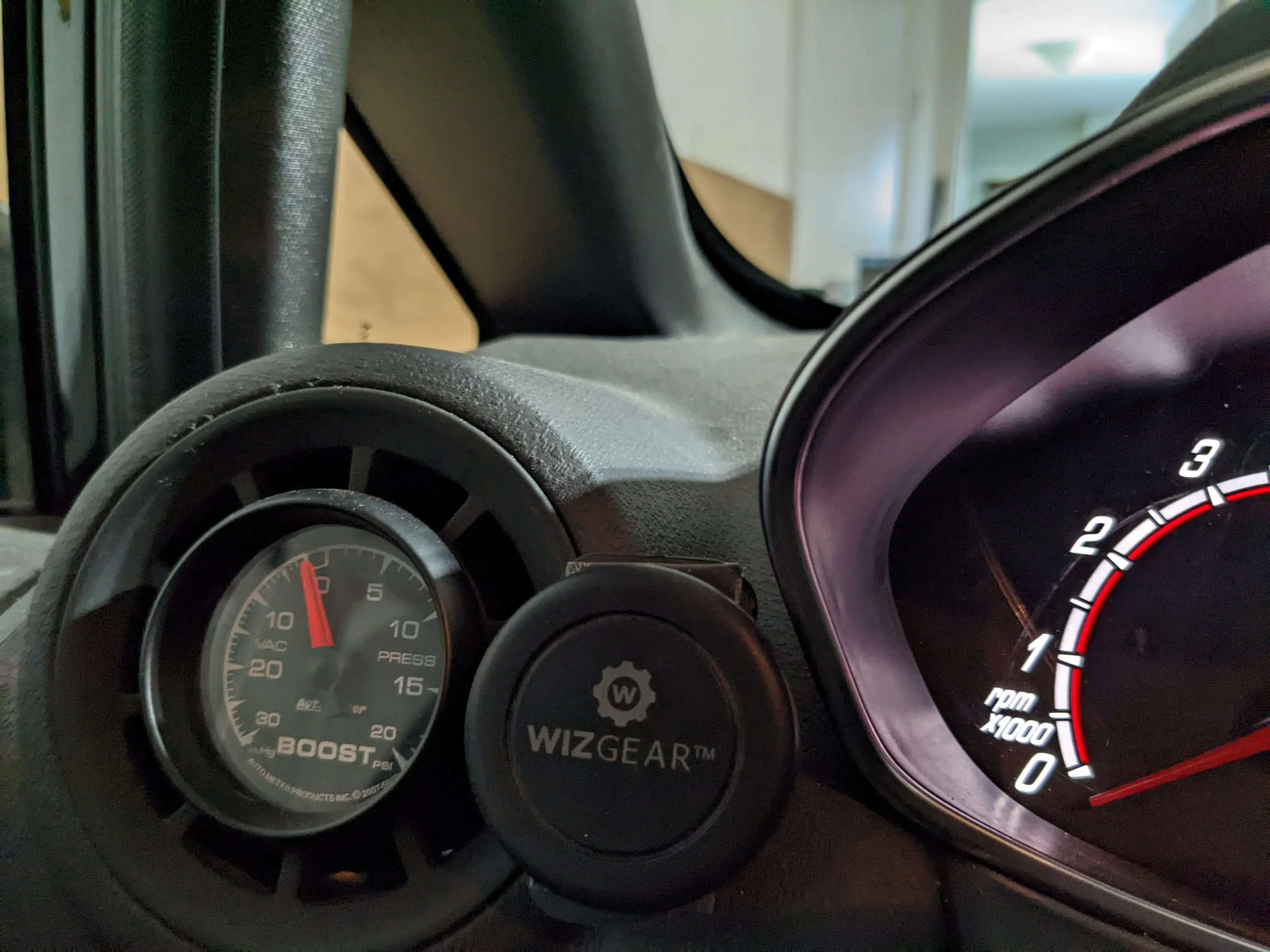 Close-up of a car dashboard showing a Boost PSI gauge, a Wizard Gear attachment, and a partly visible tachometer.