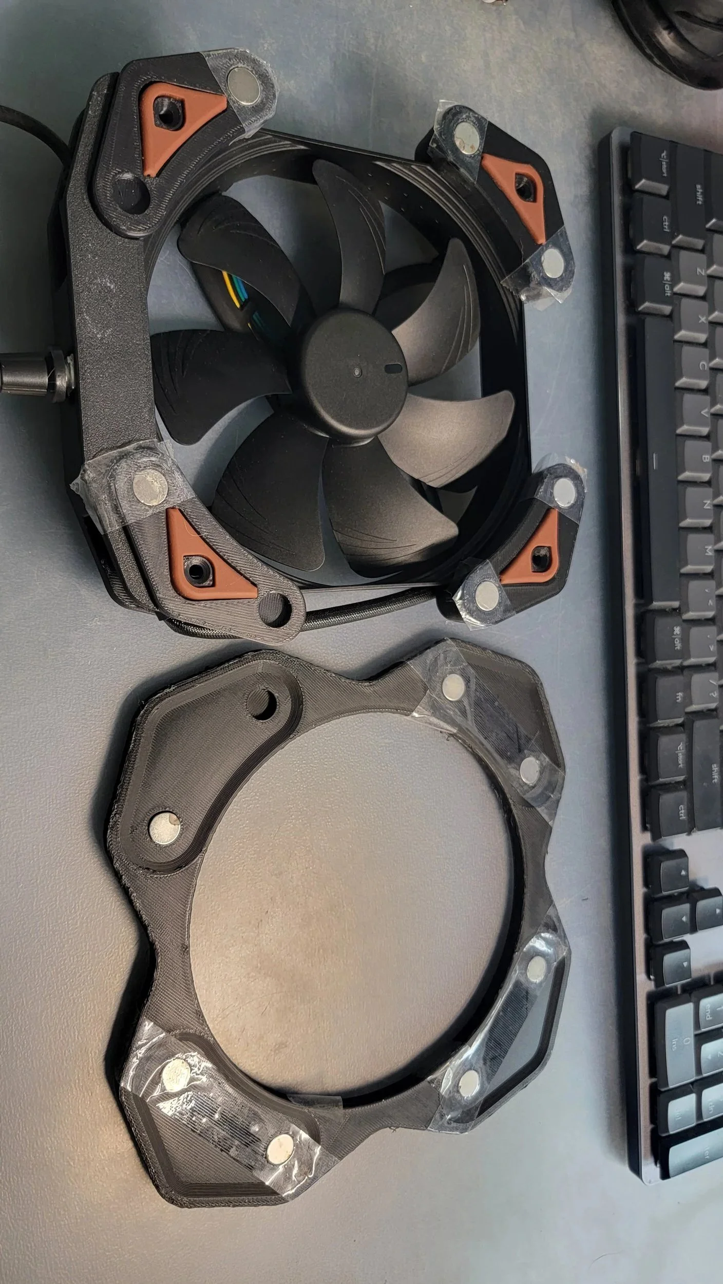 A Prototype magnet fan along with a mounting bracket, placed on a desk next to a keyboard.