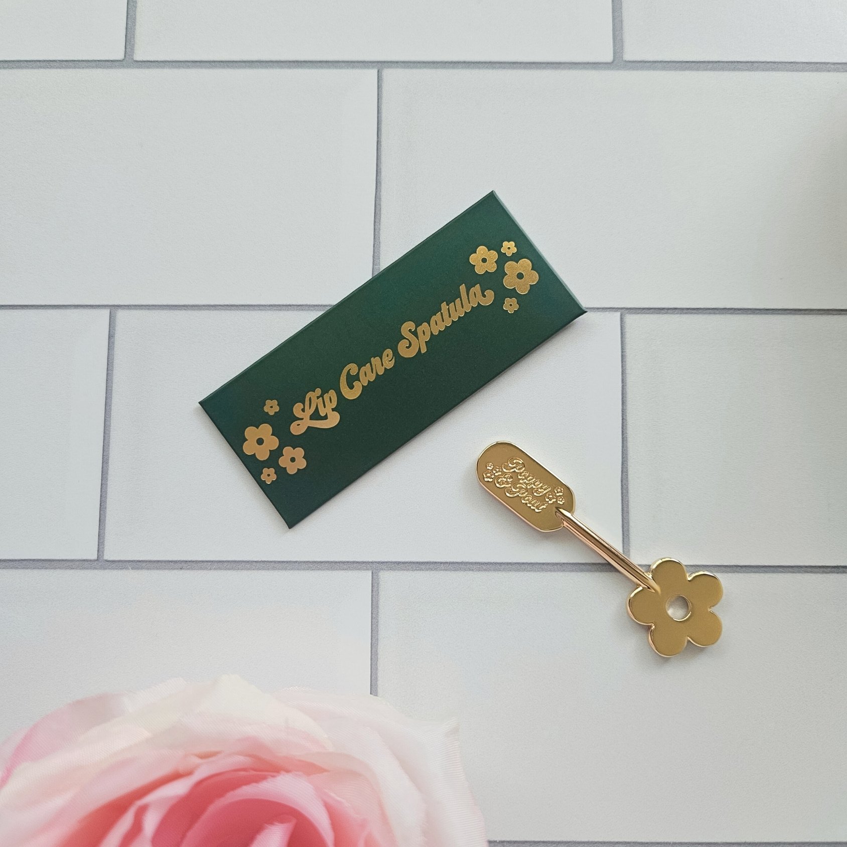 • Gold lip scrub spatula by Poppy & Pout with a flower shaped handle, perfect for clean, elegant application and a stylish gift for her.