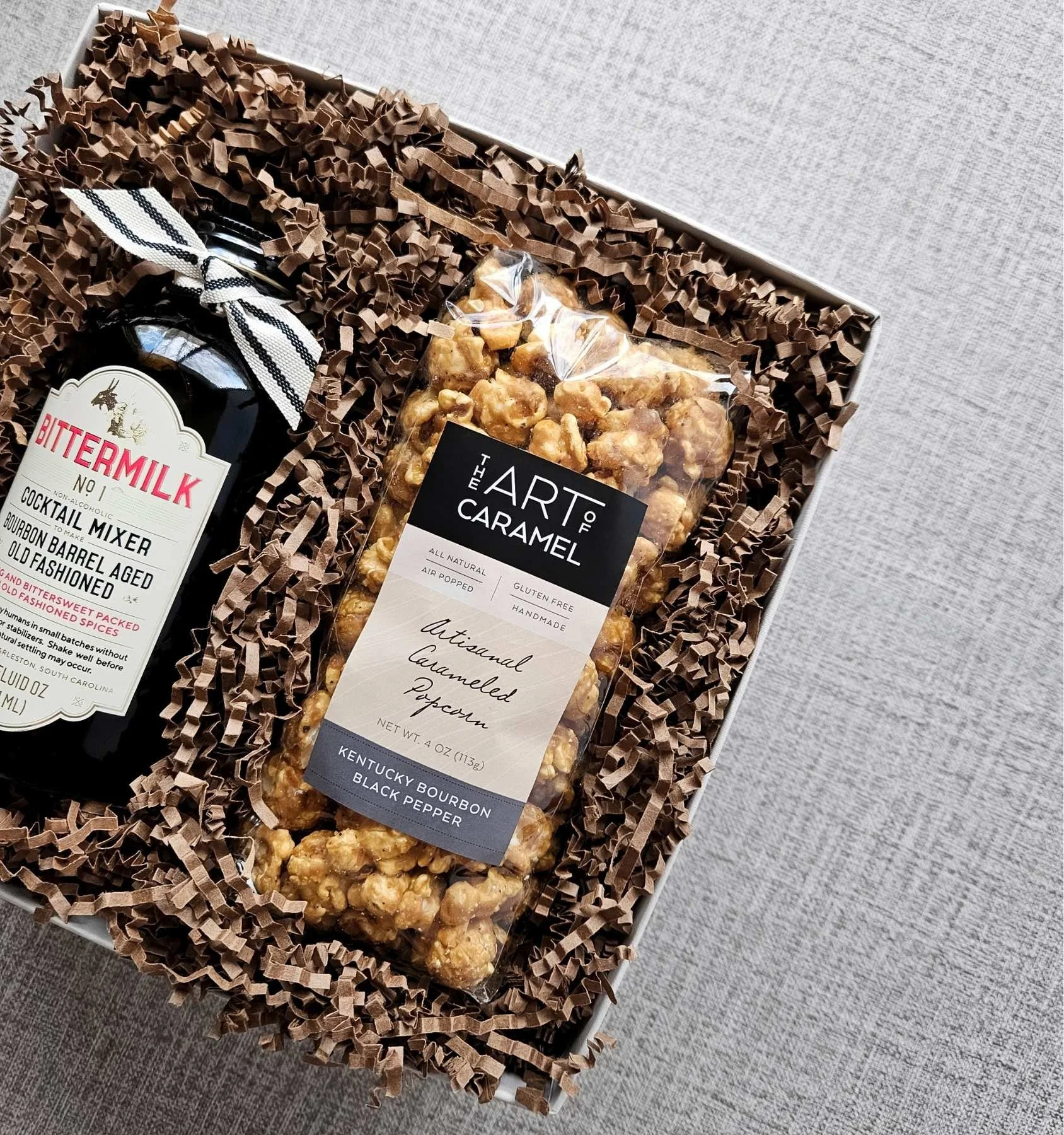 Bourbon‑inspired gift box with full‑size Bittermilk Old Fashioned mixer and Kentucky bourbon black pepper popcorn in luxury linen packaging.