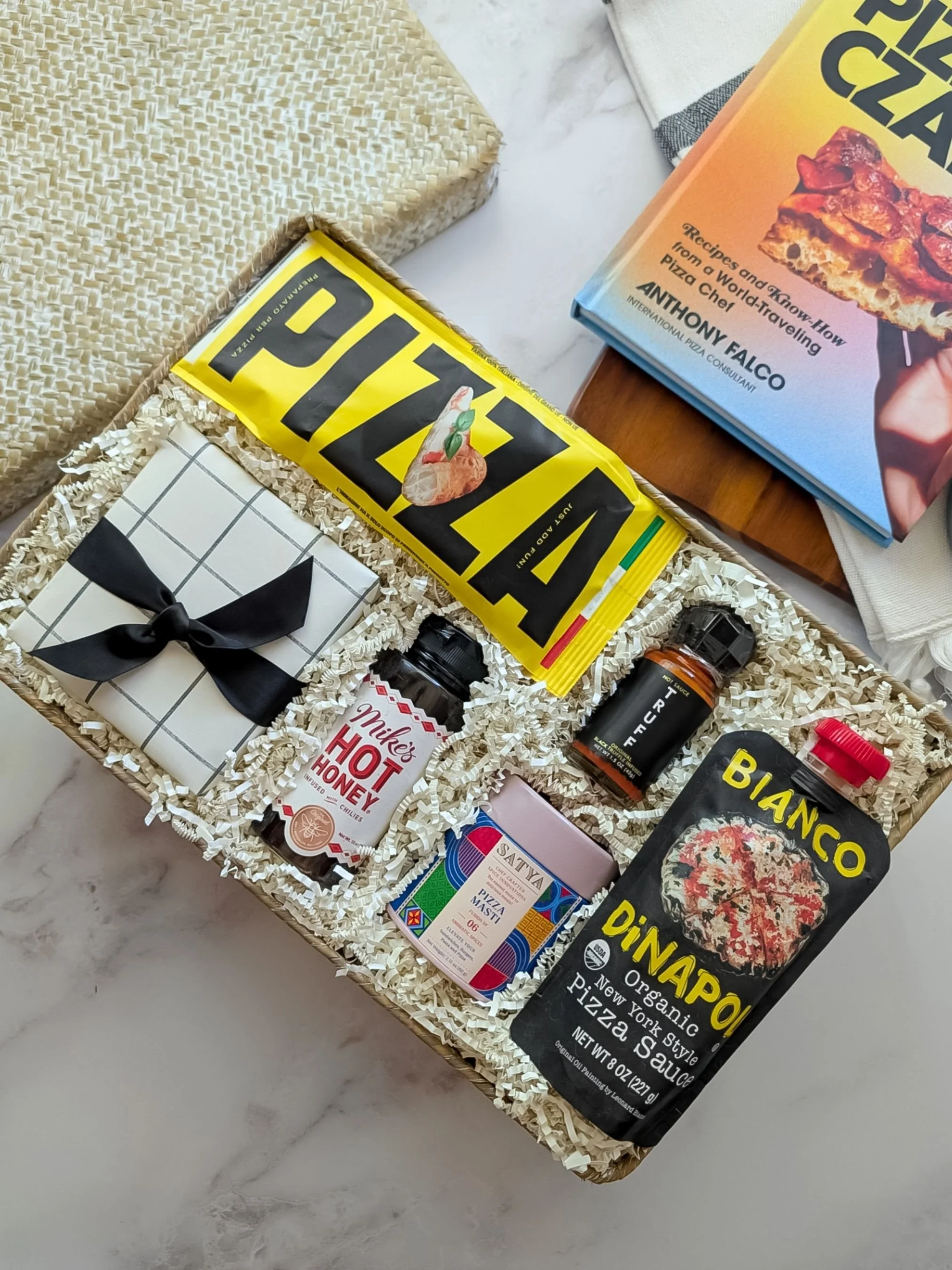 Gourmet Pizza Night basket with artisan sauce, hot honey, Truff sauce, pizza masti seasoning, dough mix, and a pizza cutter wrapped in paper in a seagrass basket