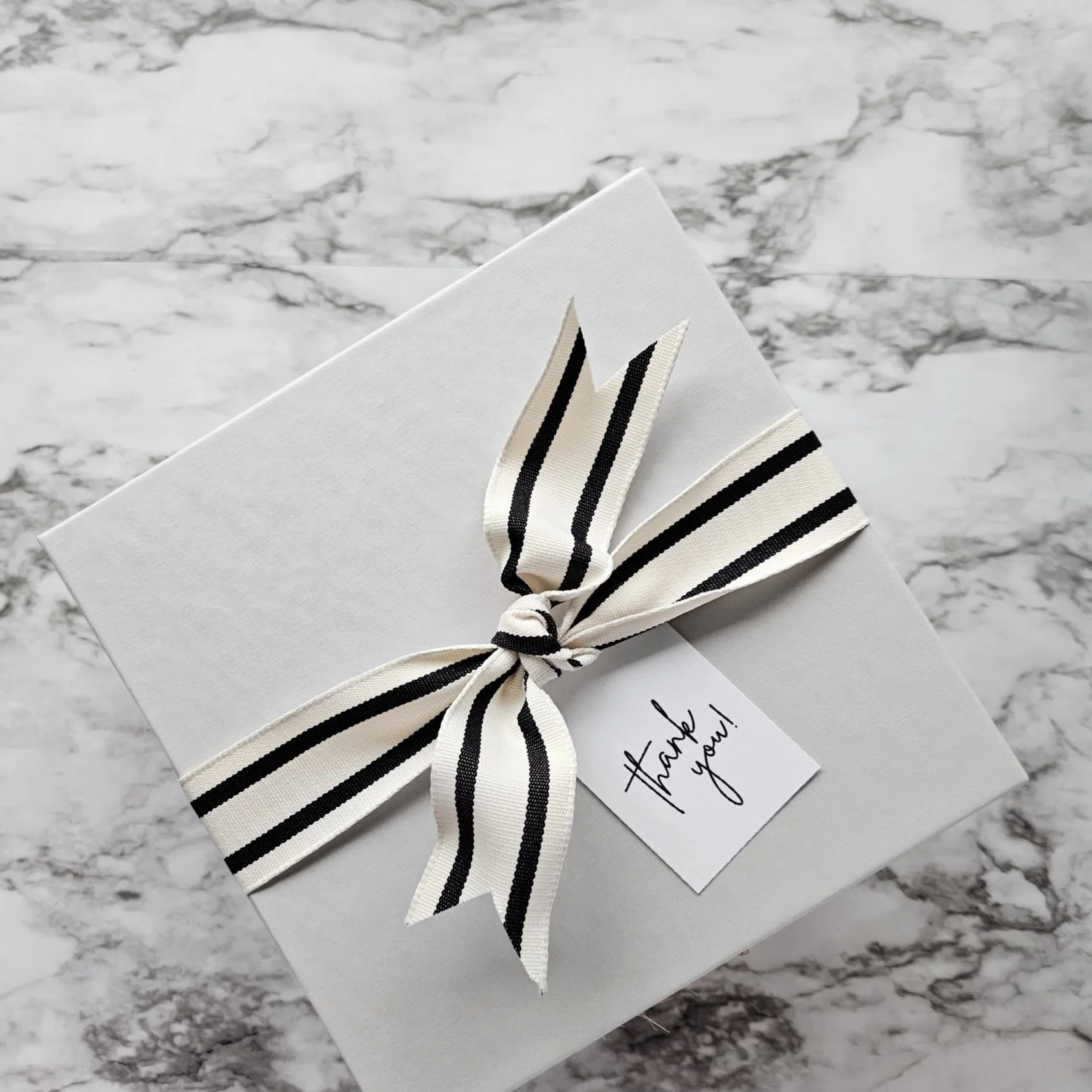 Neutral-toned striped ribbon tied elegantly on a luxe linen wrapped gift box. Complimentary gift tag and notecard for personalized message.